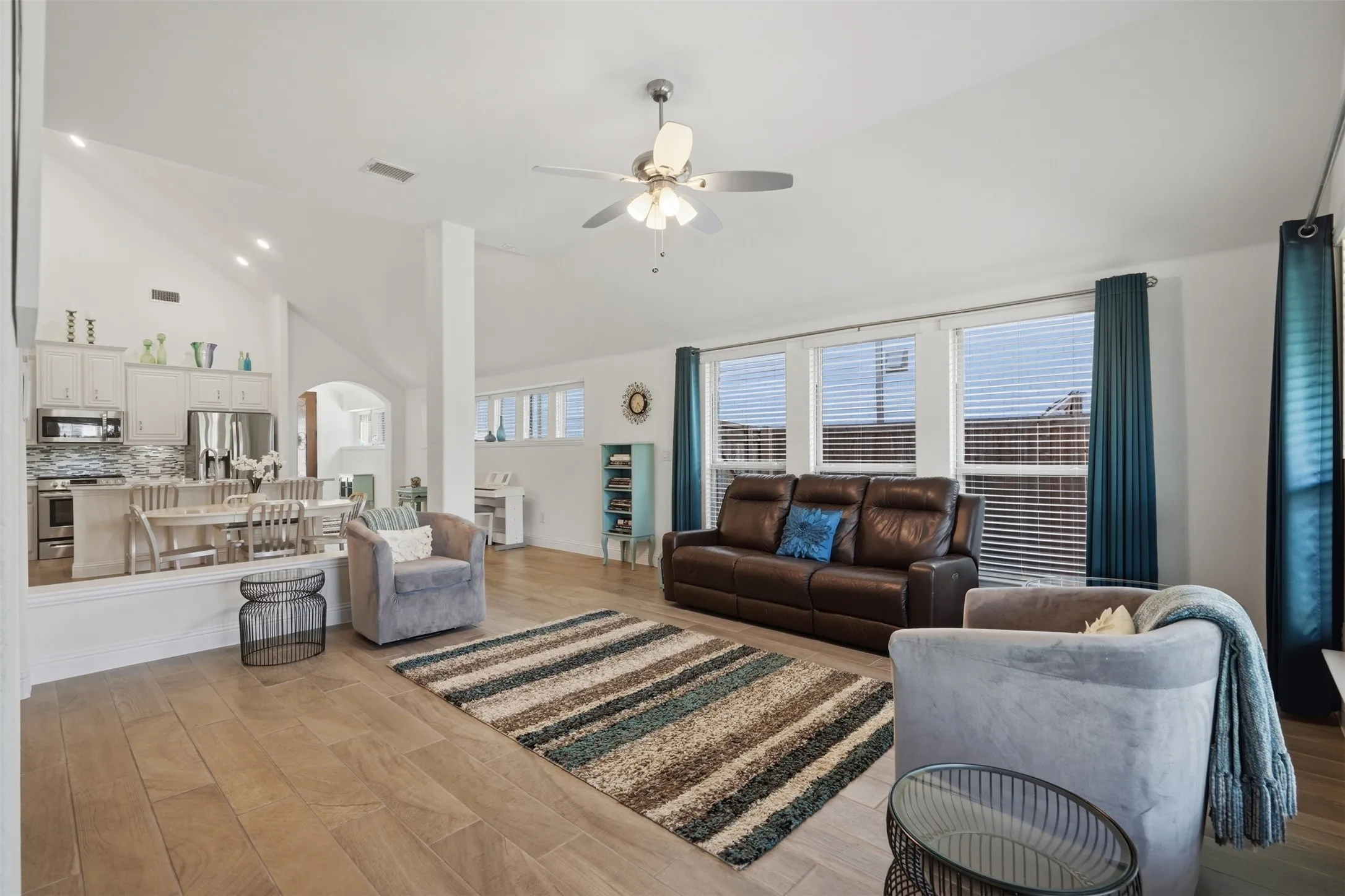Bright and inviting space featuring wood-finish flooring, recessed lighting, and multiple windows that fill the room with natural light, complemented by a well-appointed kitchen with stainless steel appliances