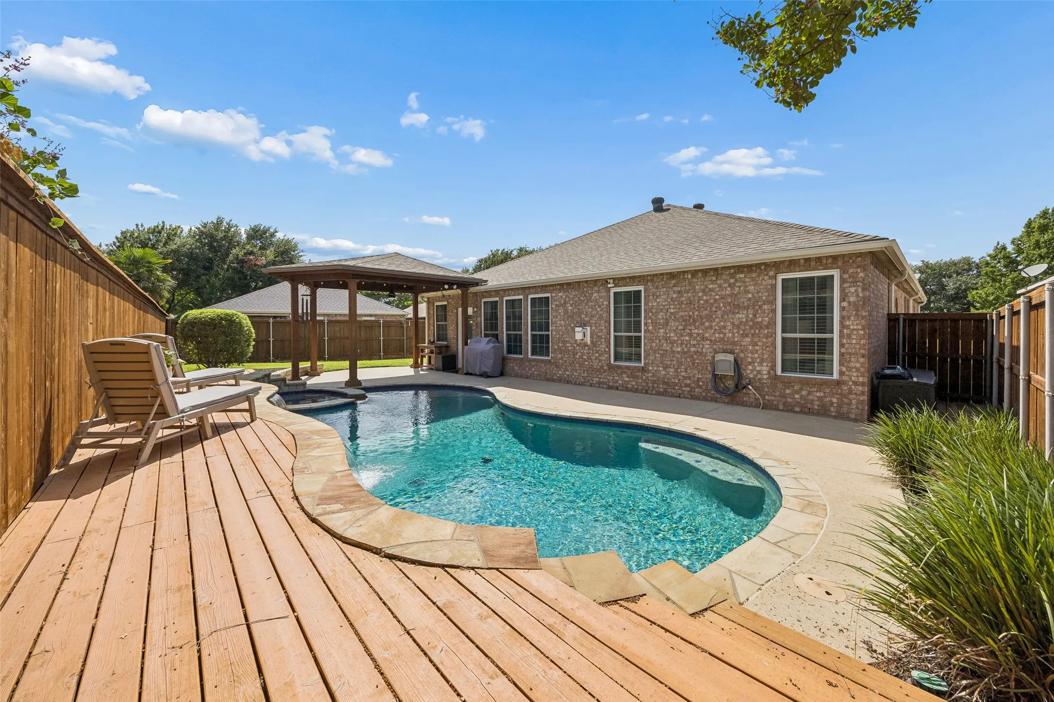 Pool, Spa, and Water Features - The freeform pool pairs with an attached spa and cascading water features, while stone accents and an elevated deck add texture and visual interest to the backyard.