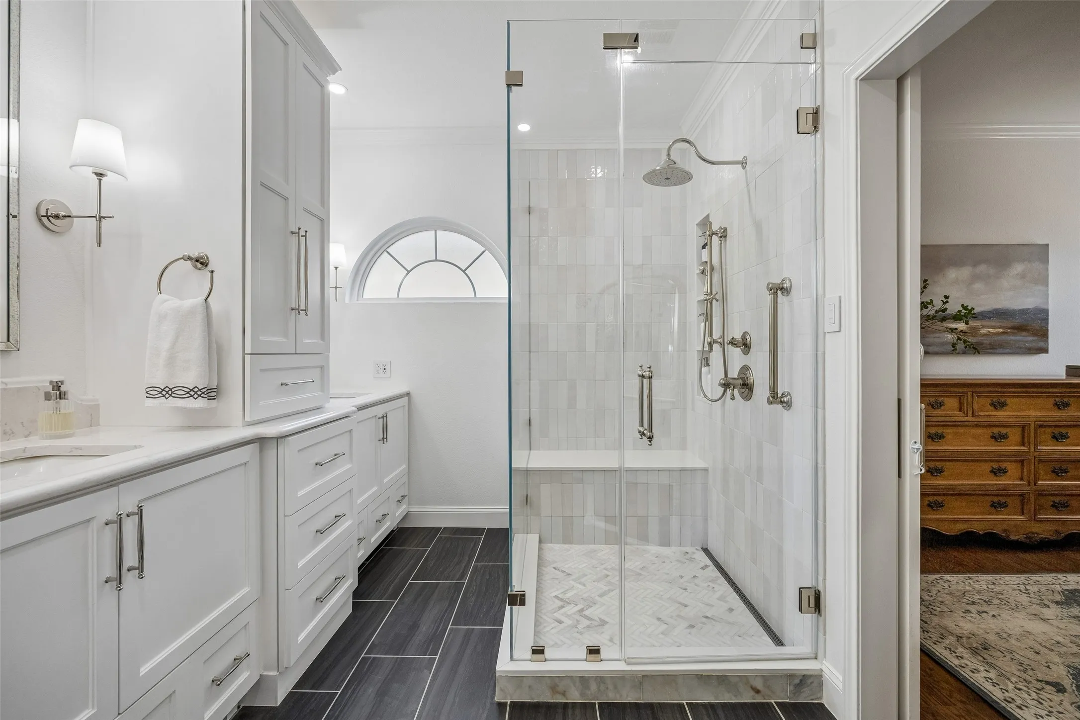 An Oversized Frameless Glass Shower - The renovated shower features a frameless glass enclosure, built-in bench, vertically set tile, and a generous rain-style showerhead for a spacious, spa-inspired experience.