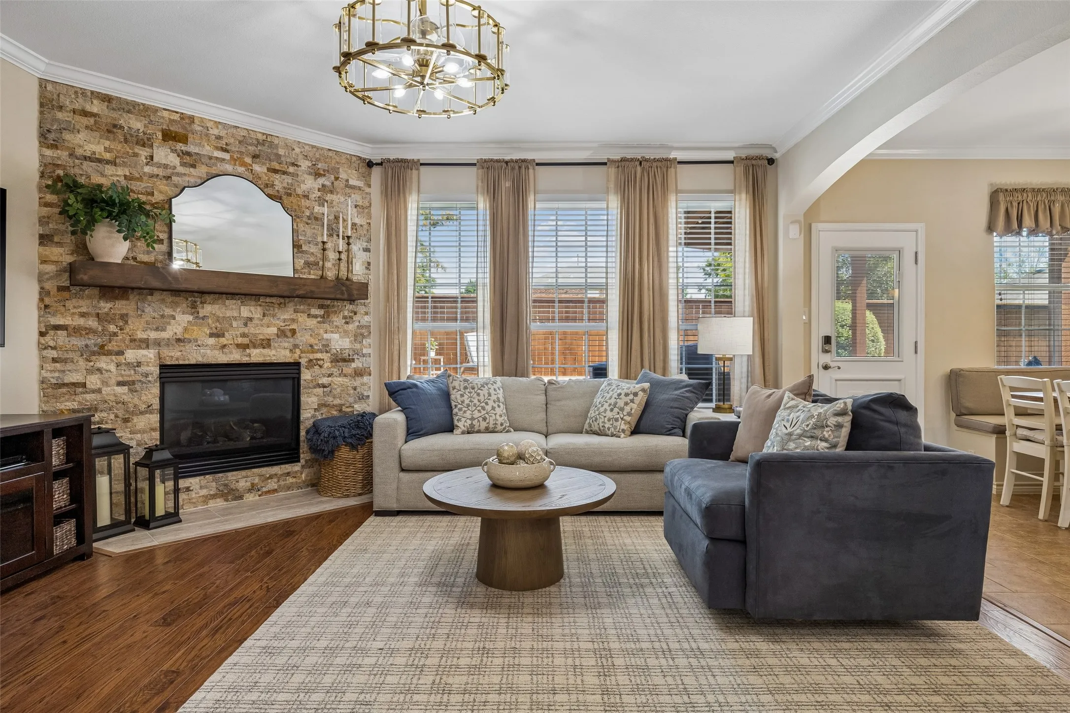 A Family Room with a Strong Focal Point - The stacked-stone fireplace and substantial mantel anchor the main living area, while a wall of windows brings in natural light and connects the room visually with the backyard.