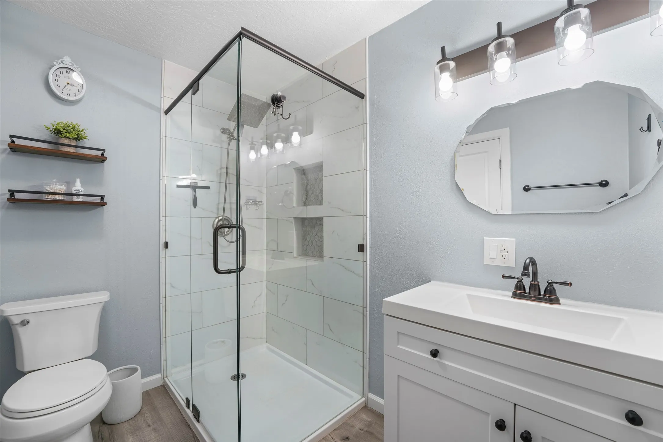 Walk-in shower with clear glass enclosure and black trim, featuring white tiled walls and built-in niches