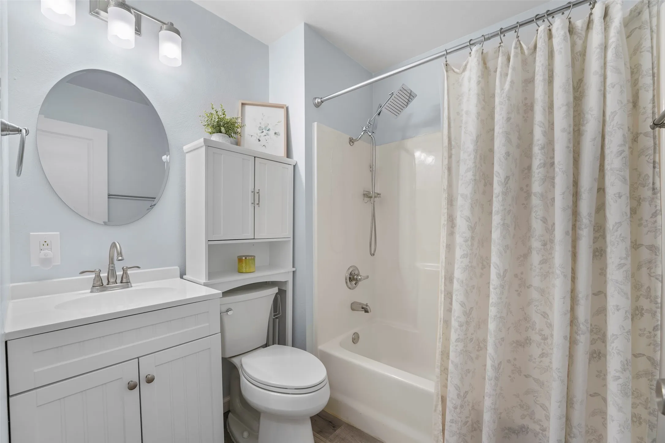 Bathroom featuring a white vanity with an integrated sink, brushed nickel faucet, wall-mounted circular mirror, and overhead lighting