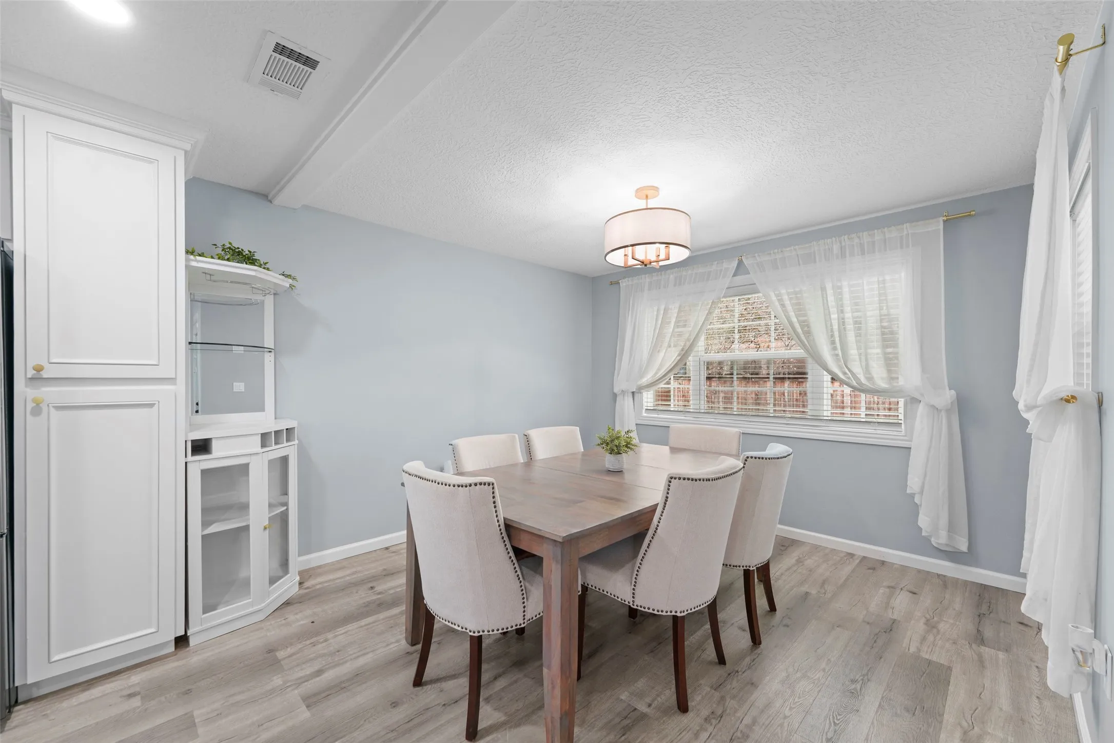 Dining area featuring wood-finish flooring, a contemporary chandelier, and a large window with white blinds