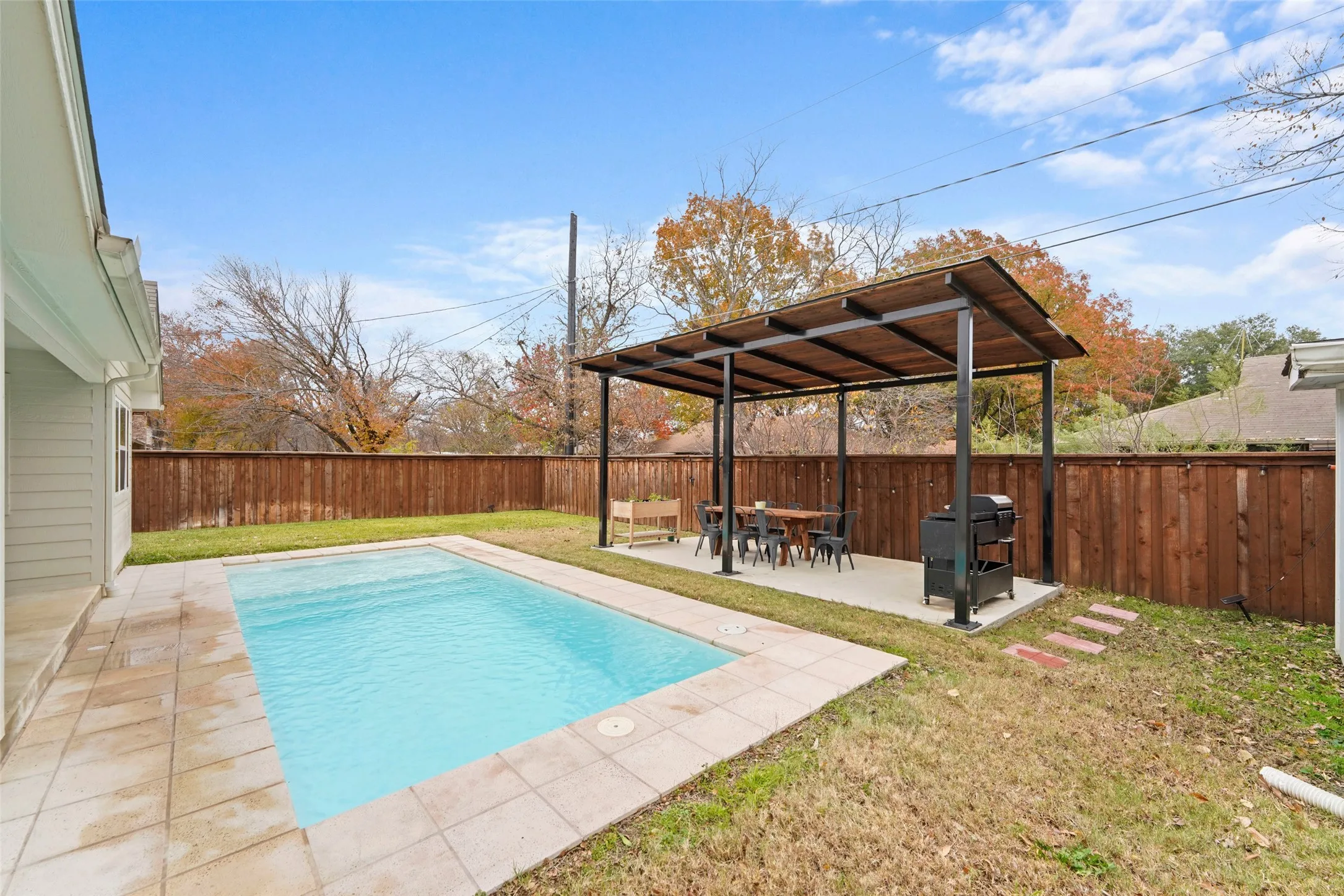 Backyard oasis featuring a swimming pool with tile surround, a covered patio with a metal frame and wood ceiling, and a wooden privacy fence