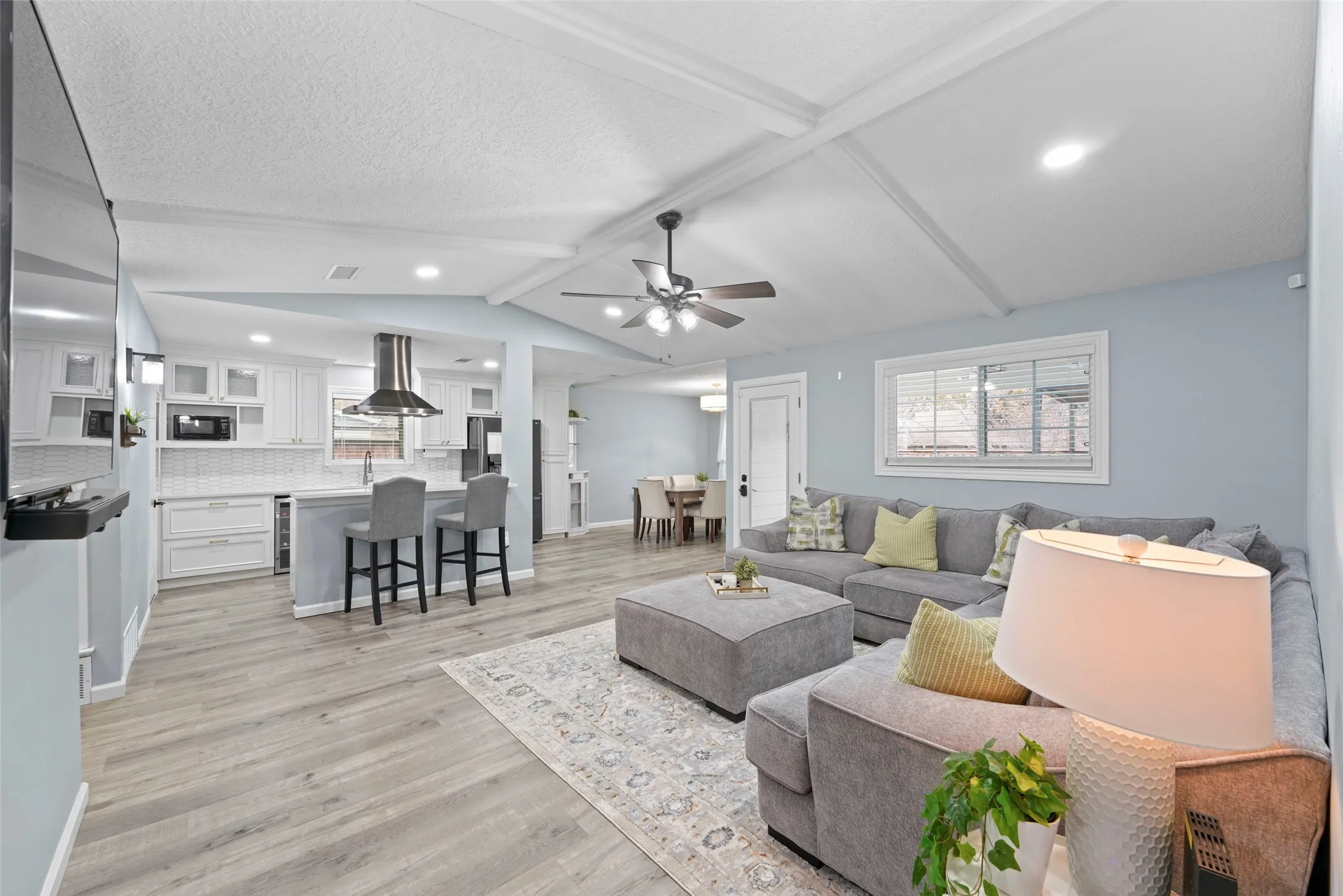 Open-concept living space featuring wood-finish flooring, a contemporary kitchen with white cabinetry and a range hood, recessed lighting, and a ceiling fan