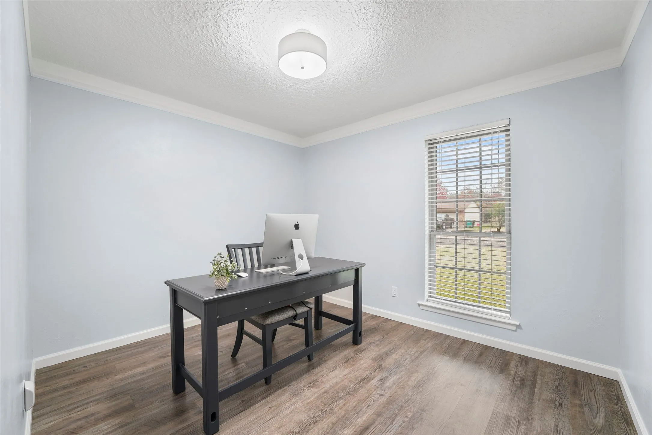 Room featuring wood-finish flooring, light blue walls, white baseboards, and white crown molding