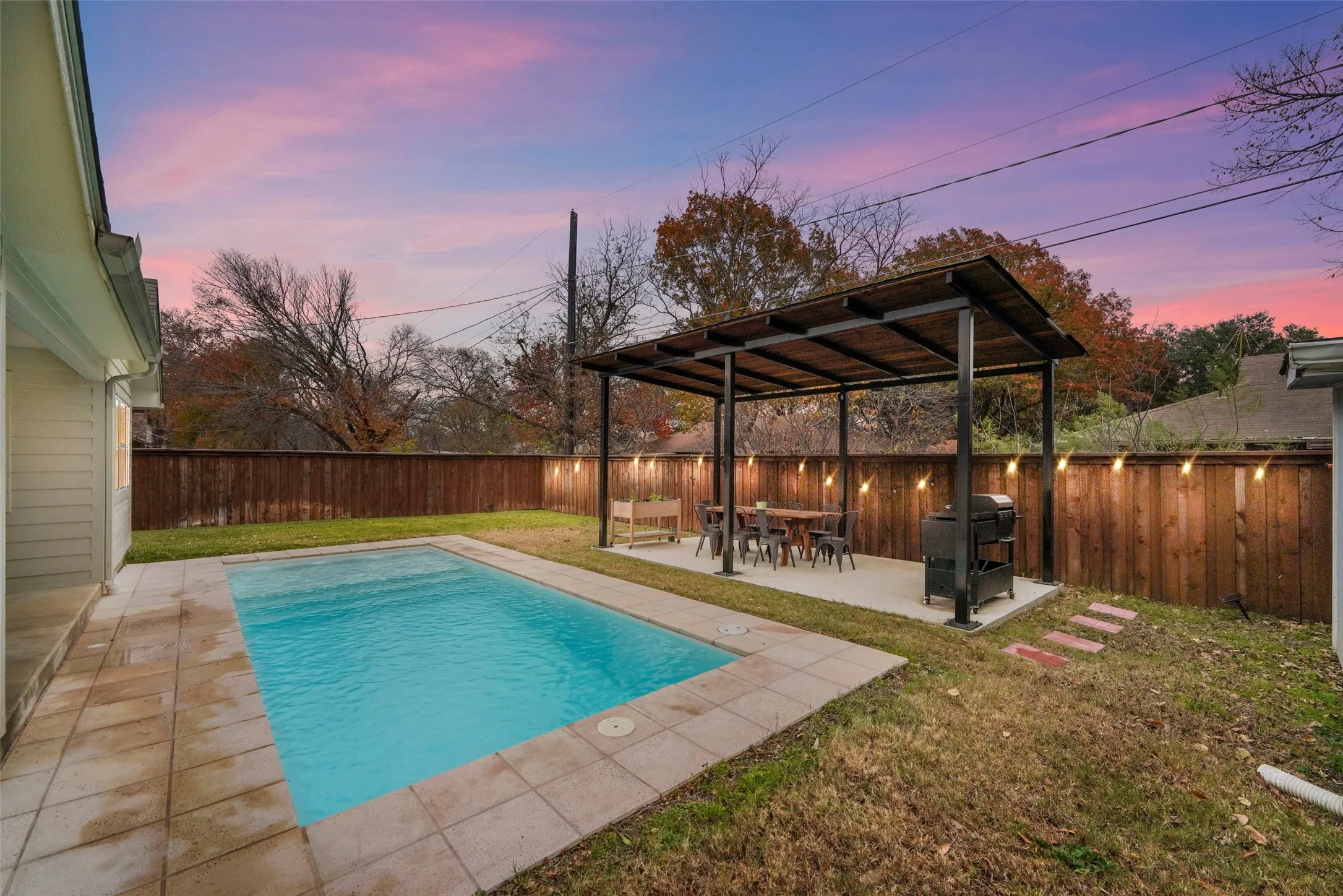 Private backyard oasis featuring a rectangular swimming pool with surrounding tile coping, a spacious covered patio with a built-in outdoor kitchen area, and a privacy fence