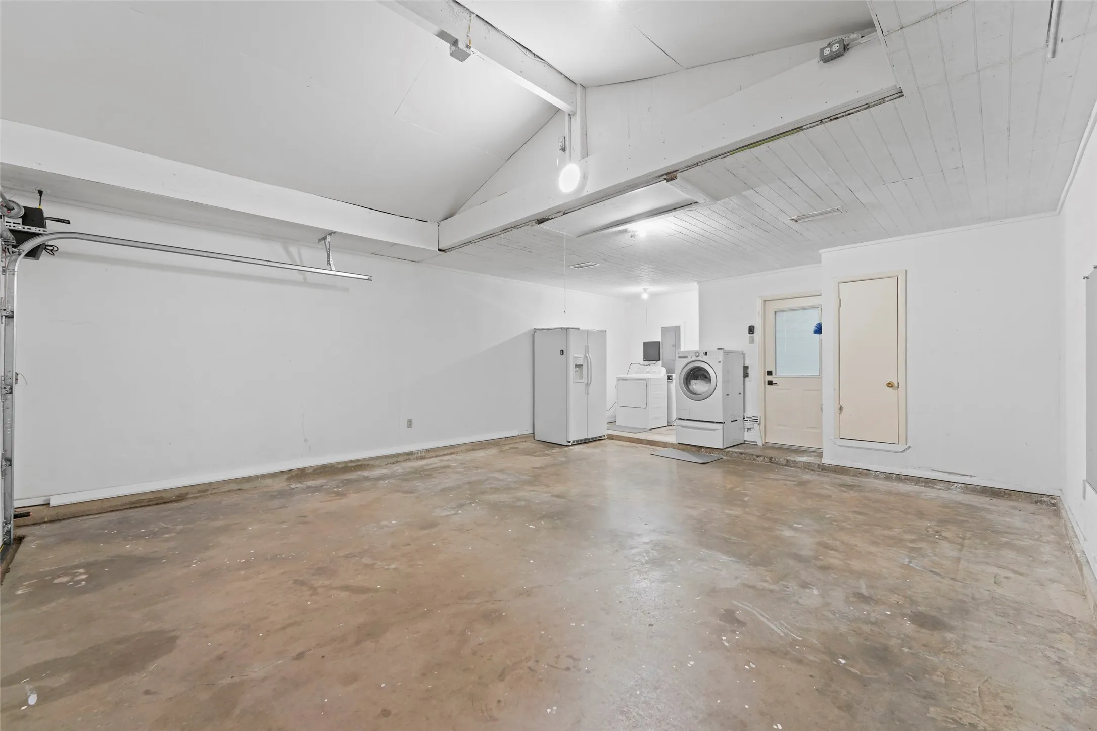 Spacious garage with concrete flooring, exposed ceiling beams, and a vaulted ceiling