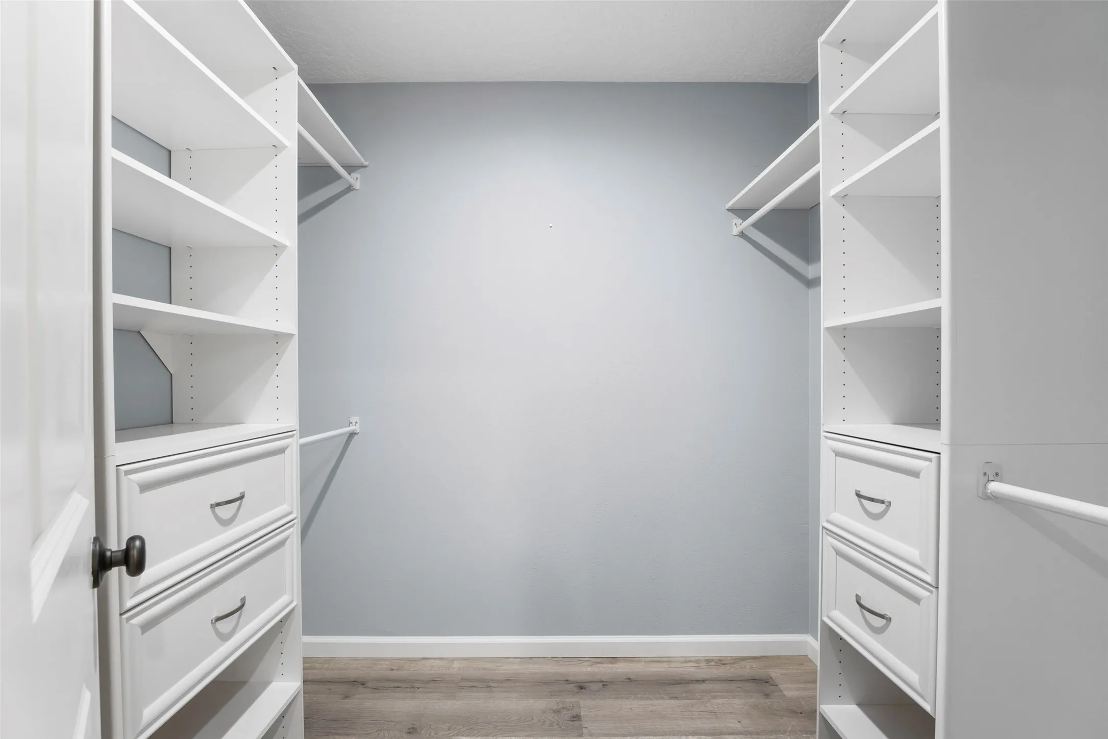 Closet featuring organized shelving, integrated drawers, hanging rods, and wood-finish flooring