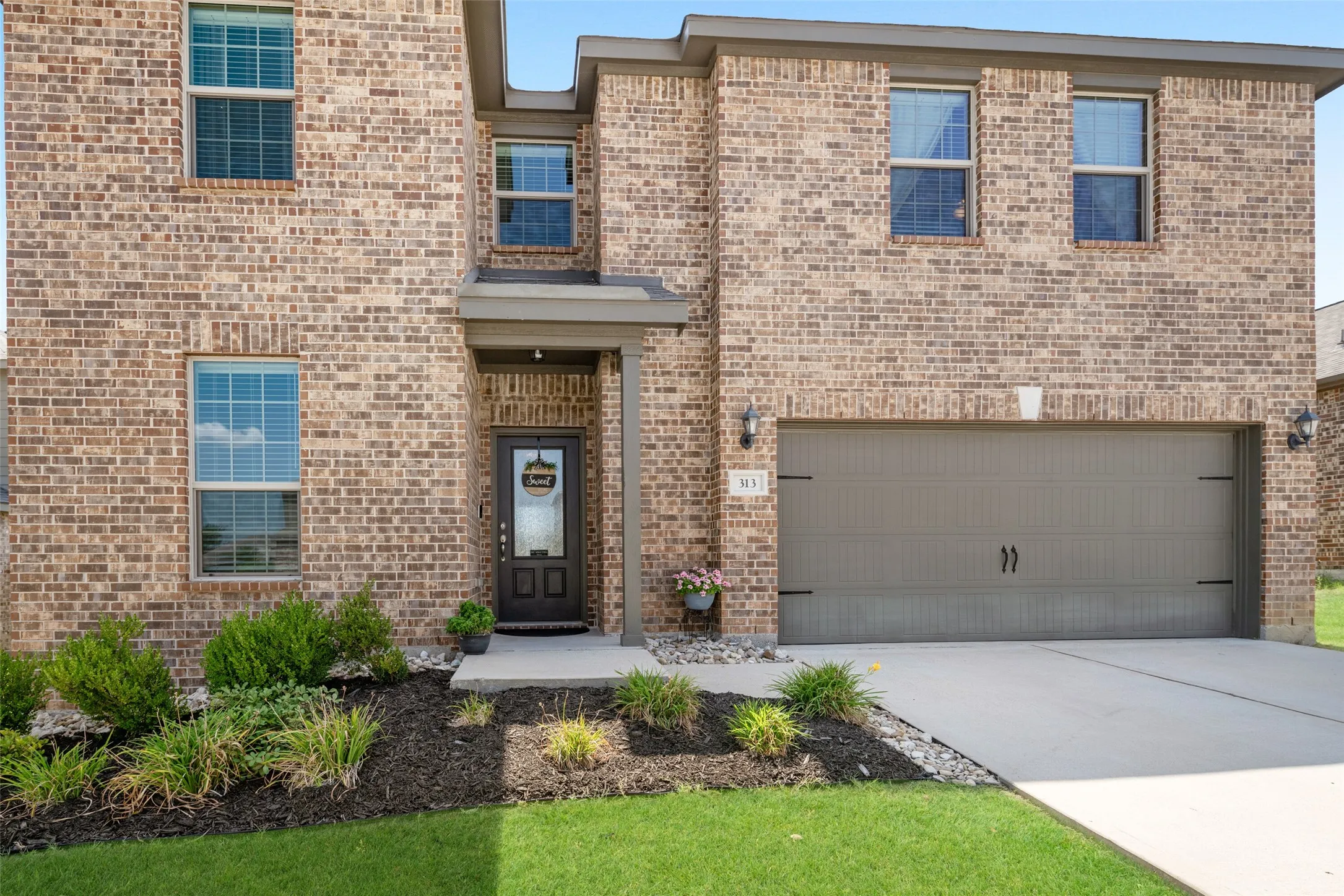 Brick exterior with a covered entry, two-car garage, and landscaped front yard