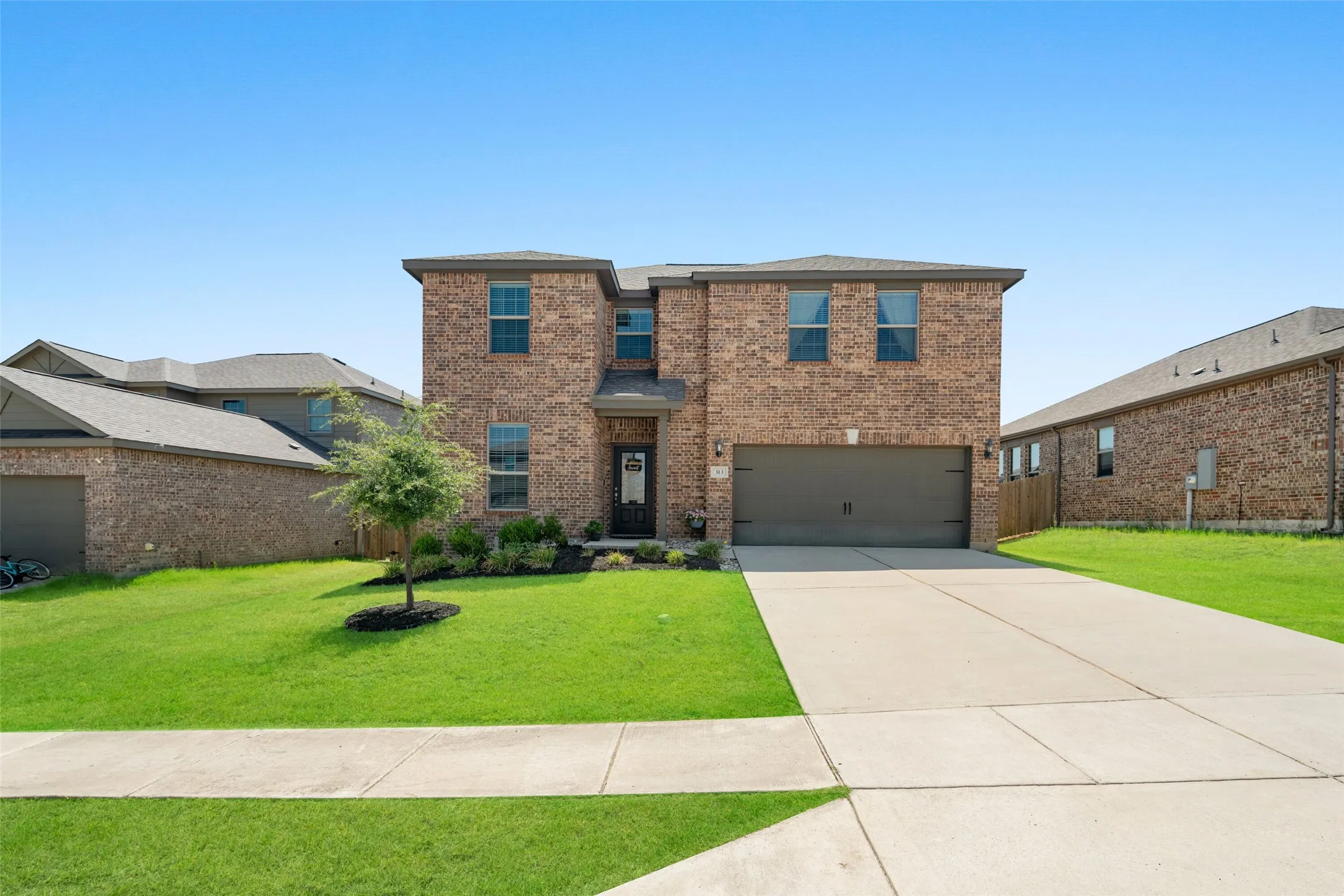 Striking two-story brick colonial with a two-car attached garage, manicured front lawn, and mature landscaping