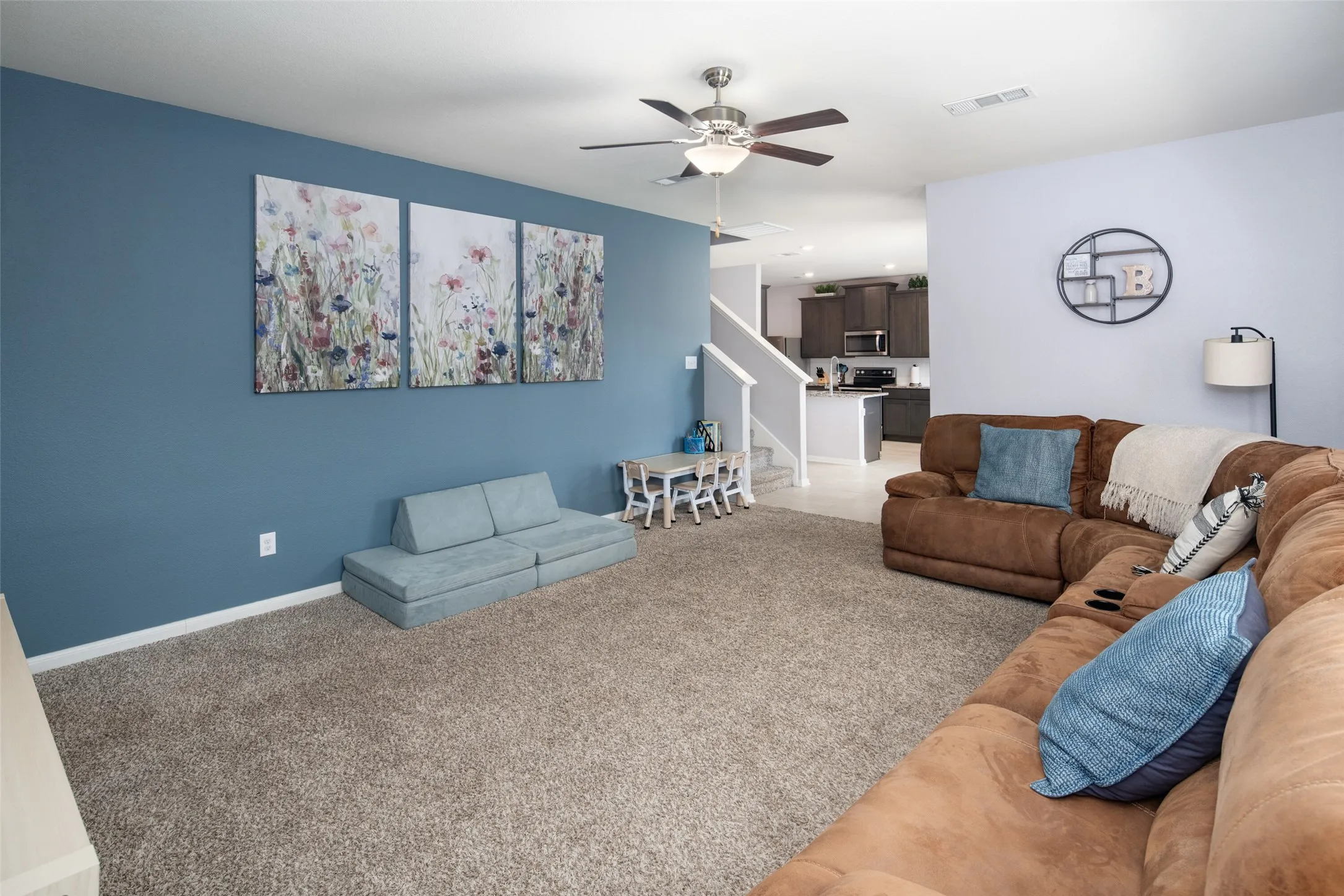 Open-concept living area featuring a ceiling fan, carpeting, and a visible kitchen space with dark cabinetry