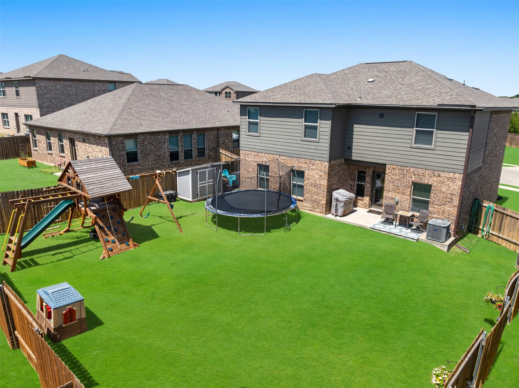 Expansive fenced backyard with a manicured lawn, brick exterior, and a rear patio