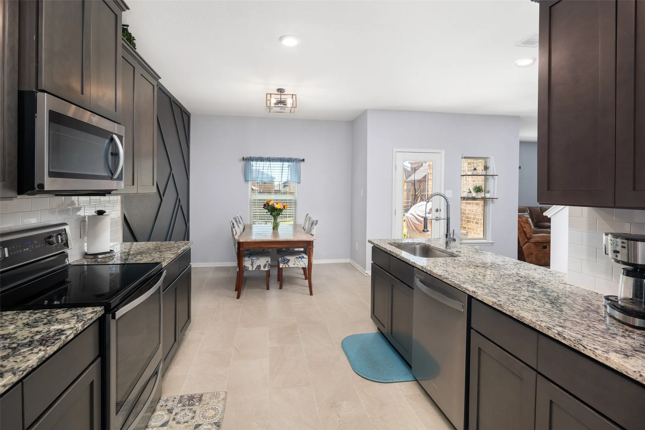 Kitchen featuring granite countertops, stainless steel appliances, dark wood cabinetry, a subway tile backsplash, and light tile flooring