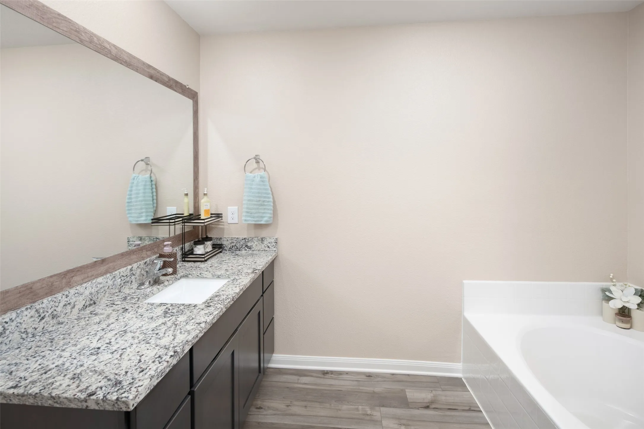 Spa-inspired primary bathroom featuring dual vanities with polished stone countertops, dark cabinetry, brushed nickel sconces, and an oversized soaking tub