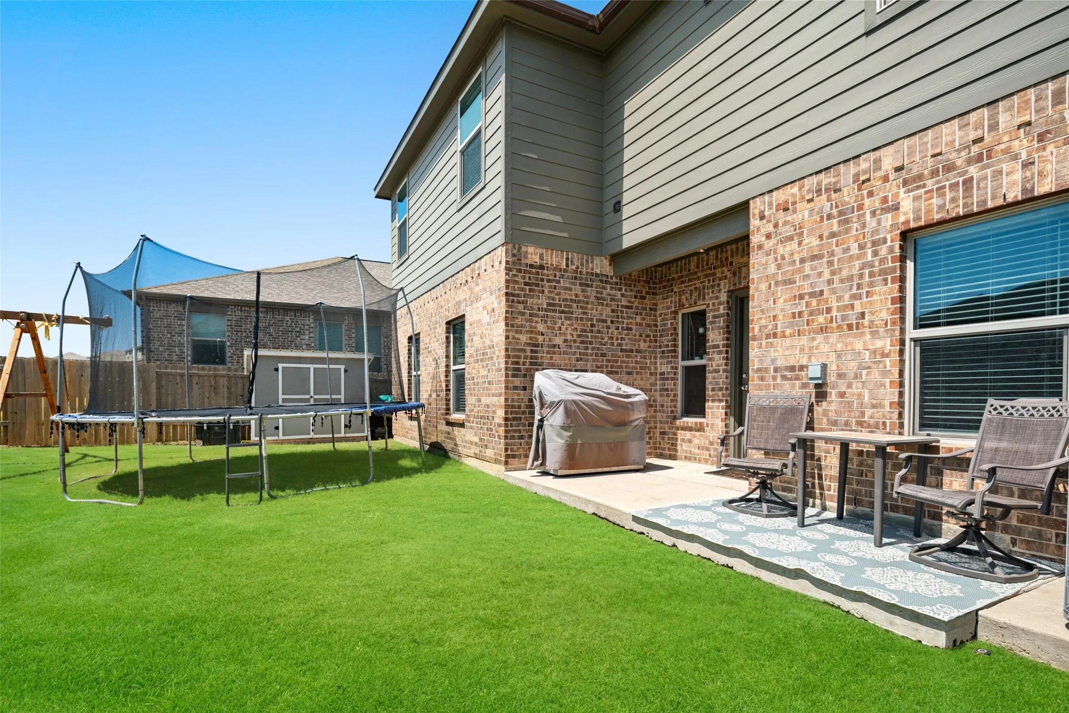 Expansive backyard featuring a manicured lawn, a concrete patio, and a brick and siding exterior