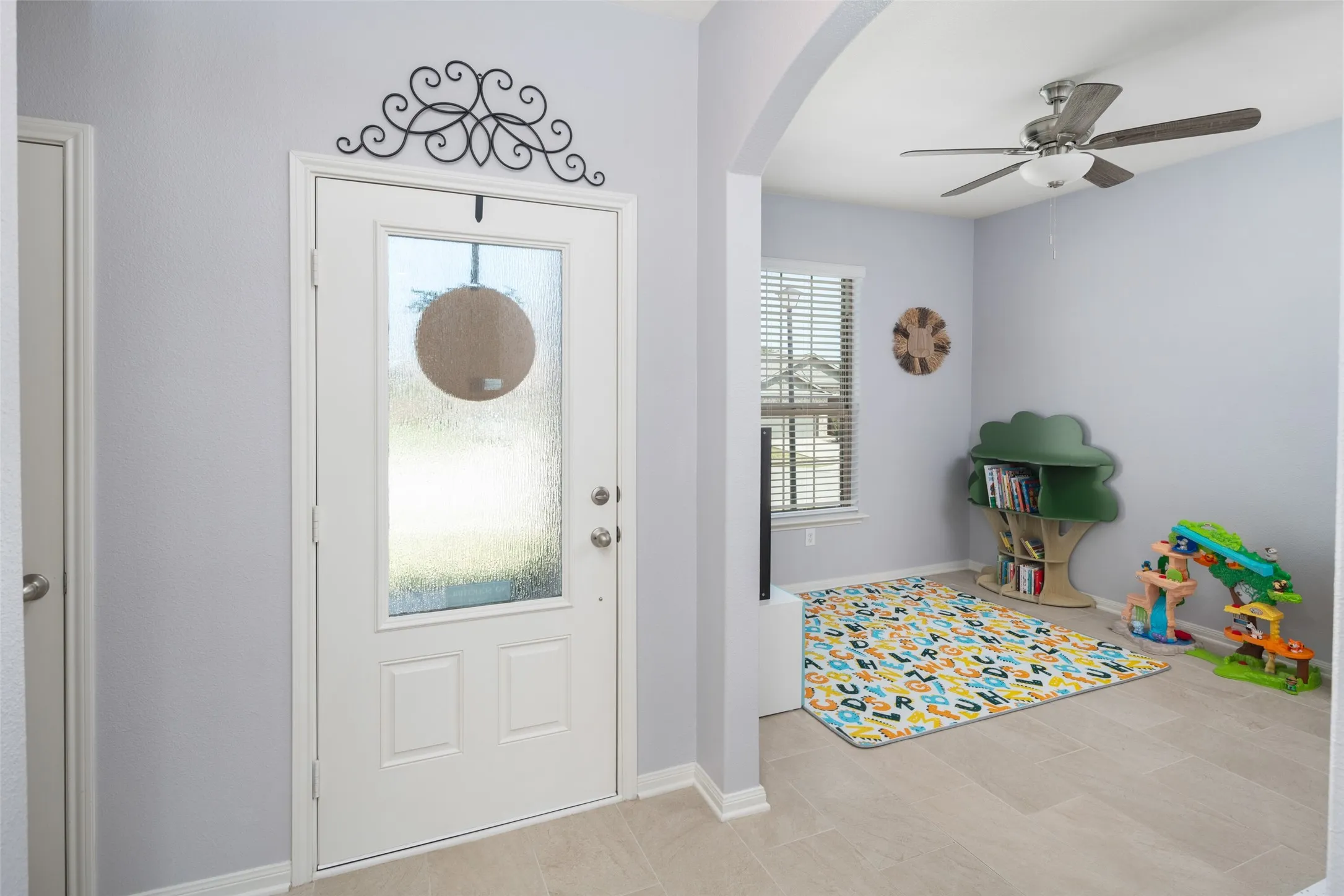 Bright, light-filled entryway featuring a white six-panel door with decorative wrought-iron transom, circular window detail, and neutral wood-finish flooring