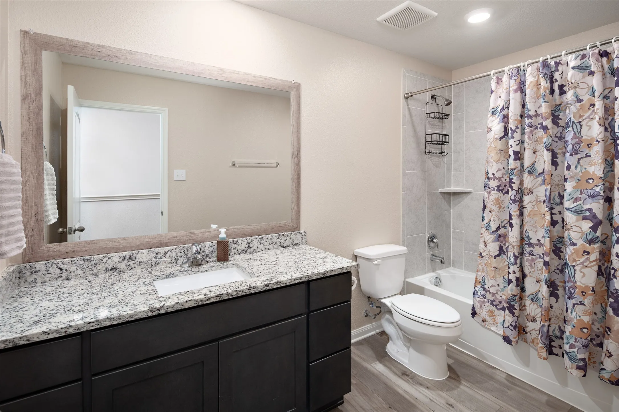 Spa-inspired bathroom featuring a dark cabinetry vanity with a speckled quartz countertop, an oversized framed mirror, and brushed nickel hardware