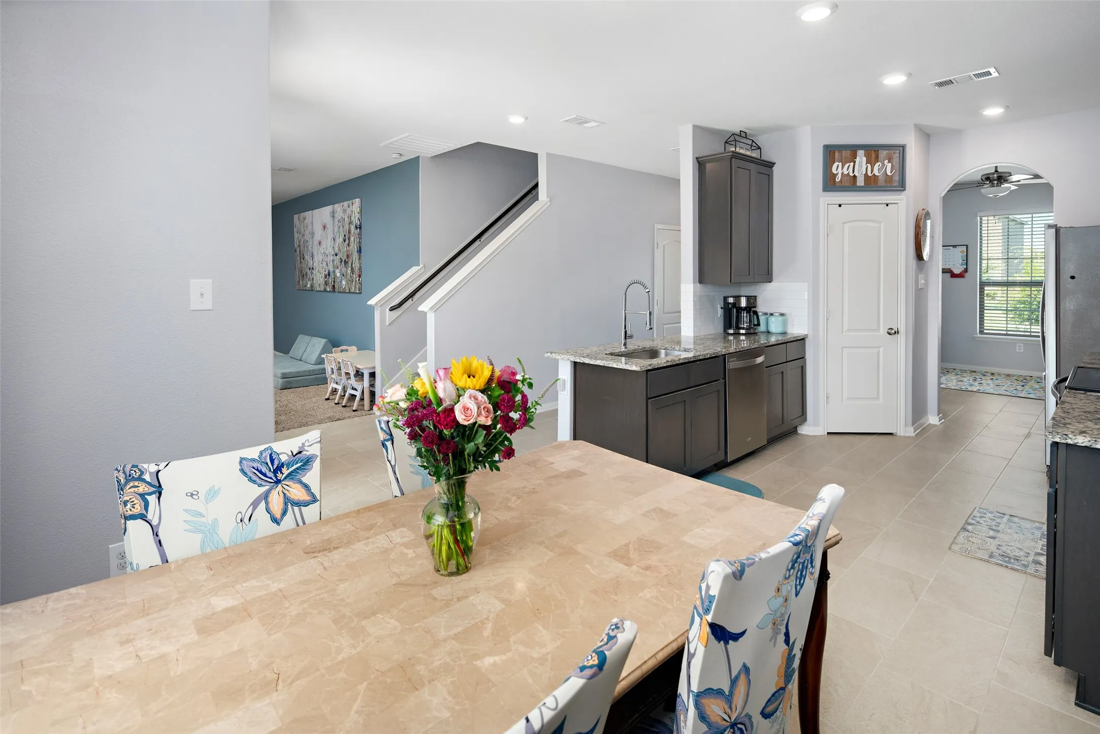 Open-concept kitchen and dining area featuring light wood-finish flooring, a substantial center island with dark cabinetry and undermount sink, stainless steel appliances, and recessed ceiling lighting