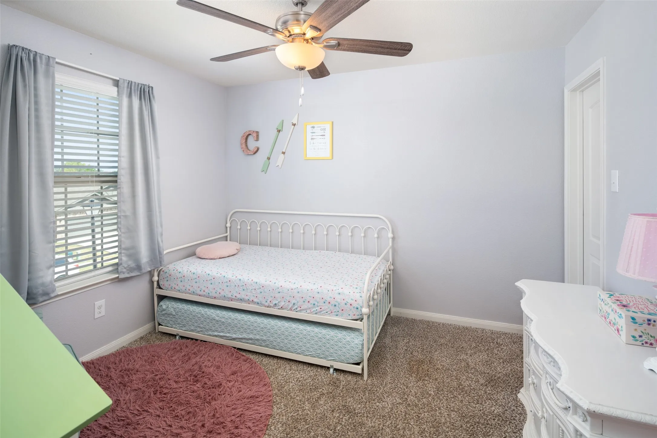 Bright secondary bedroom featuring carpet flooring, ceiling fan with integrated lighting, metal bed frame, and shuttered window with natural light