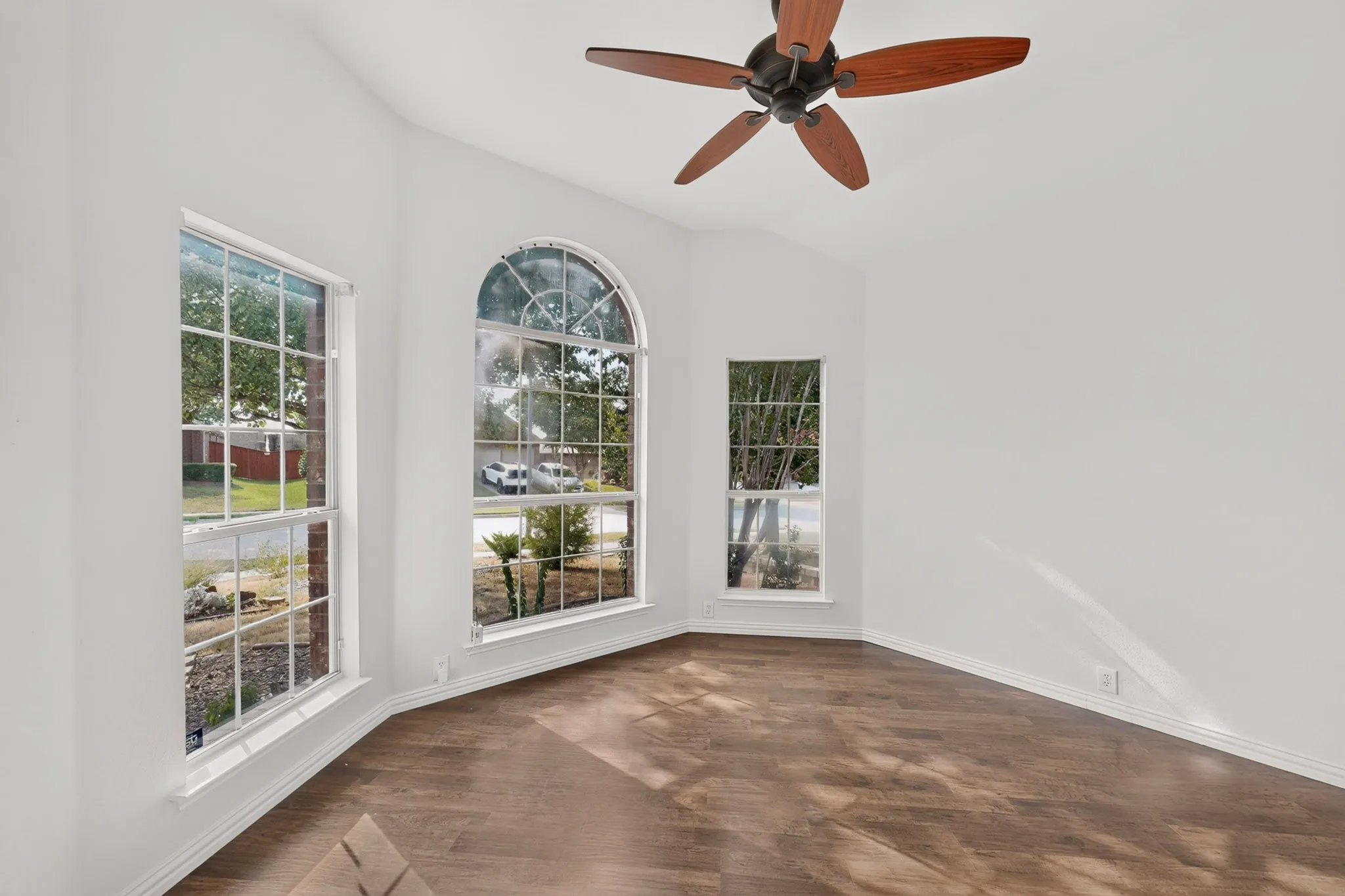 Vaulted ceiling, ceiling fan with wood-finish blades, three windows, arched window, and wood-finish flooring