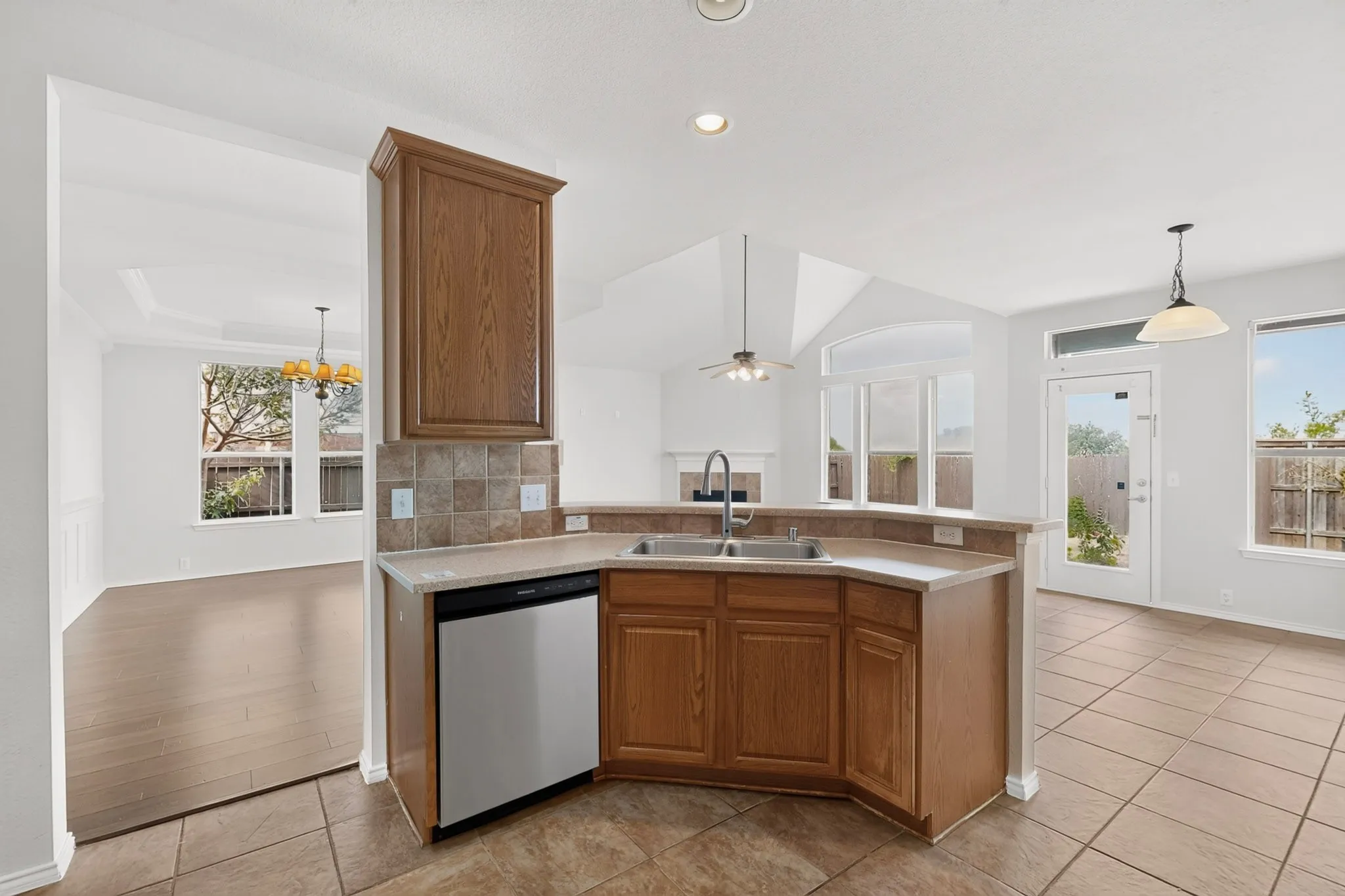Kitchen featuring a stainless steel dishwasher, double basin sink, tile backsplash, and wood cabinetry