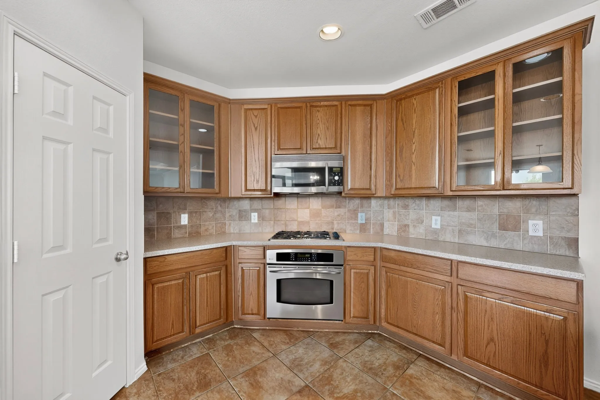 Kitchen featuring wood cabinetry, stainless steel appliances, tiled flooring, and a tiled backsplash