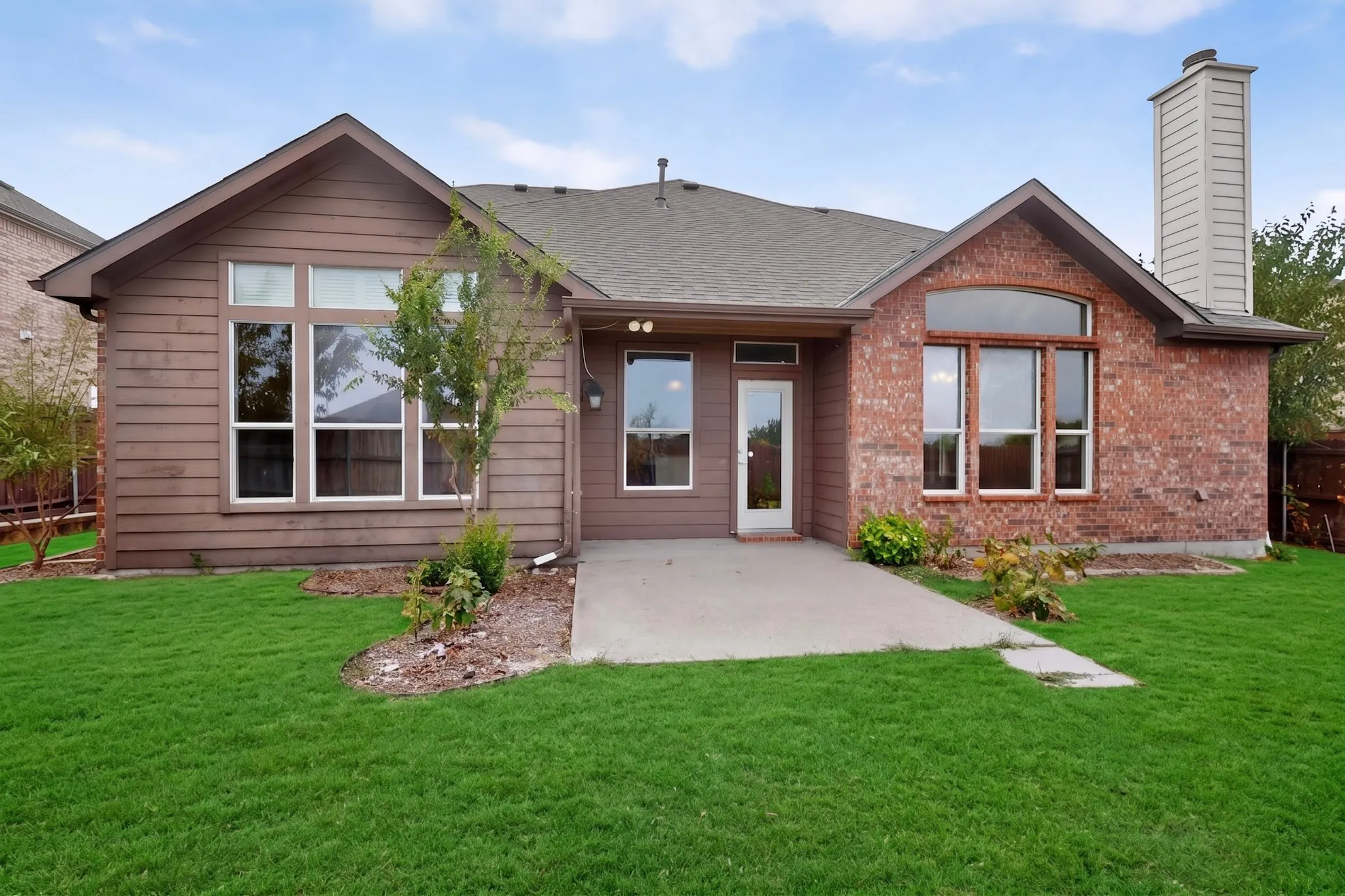 Exterior featuring brick and horizontal siding, multiple windows, a concrete patio, and a chimney