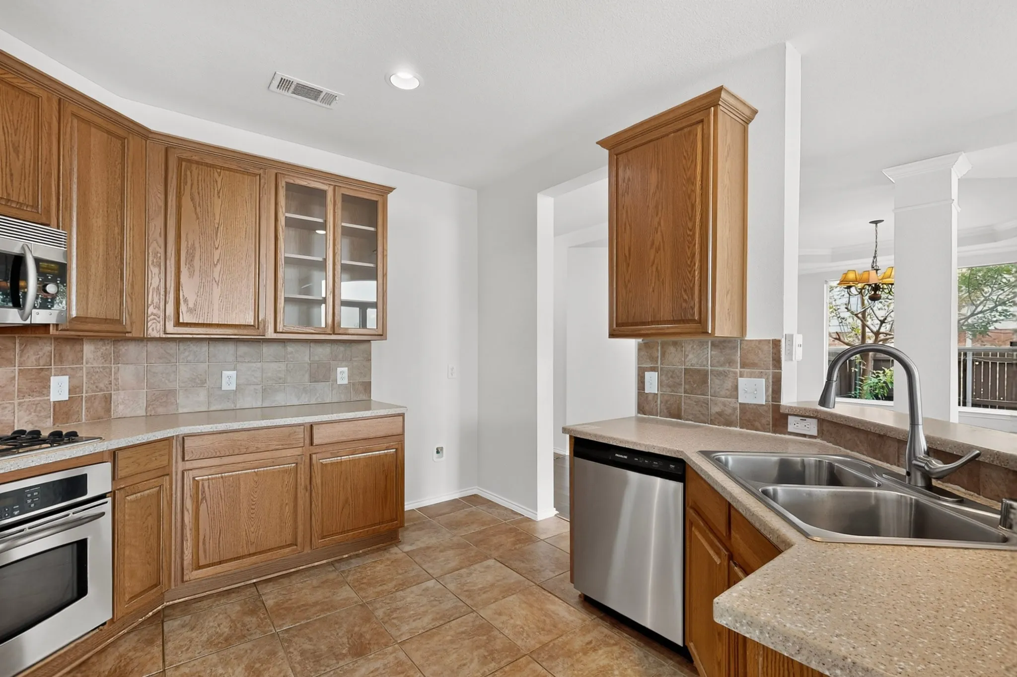 Kitchen featuring wood cabinetry, stainless steel appliances, tile flooring, stone-finish countertops, and a tile backsplash