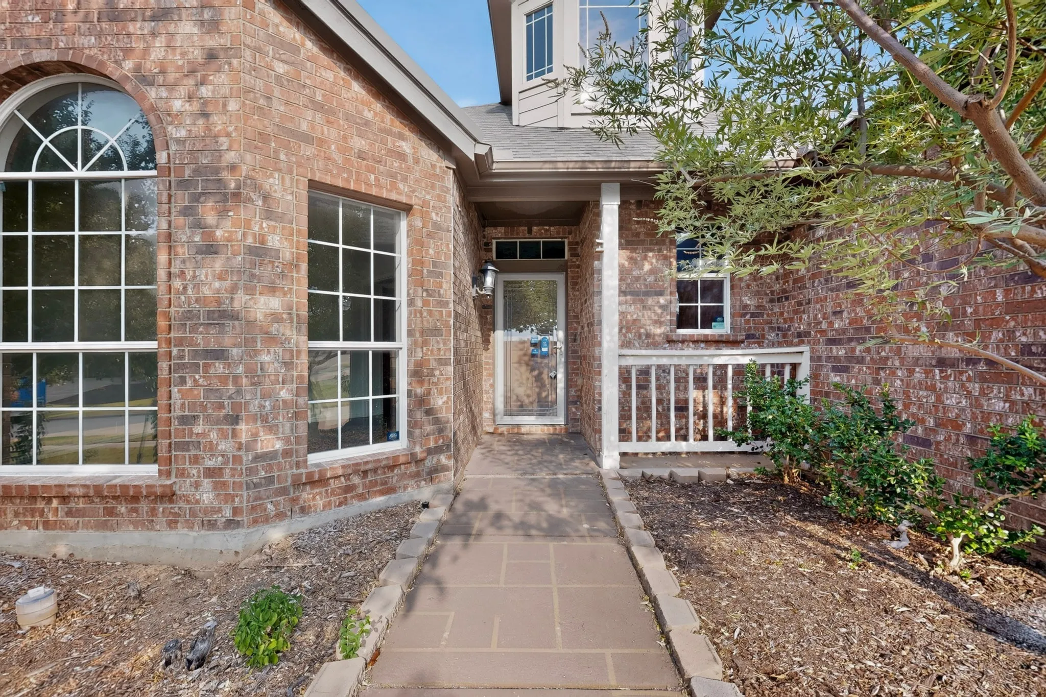 Brick exterior with an arched accent window, a covered entry, and a white wood railing