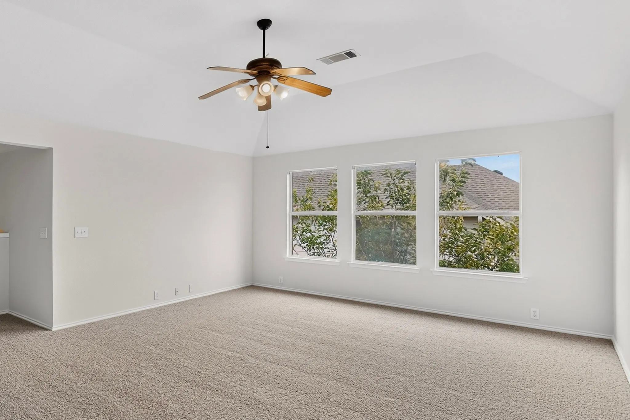 Vaulted ceiling, ceiling fan with integrated lighting, three windows, light neutral wall color, and carpet flooring