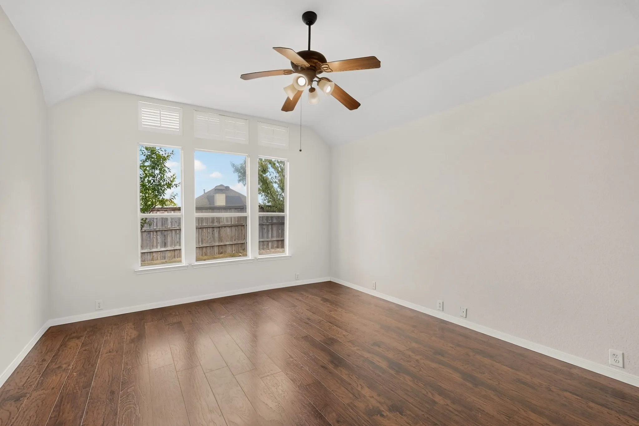 Vaulted ceiling with a ceiling fan, wood-finish flooring, and multiple windows with upper transoms