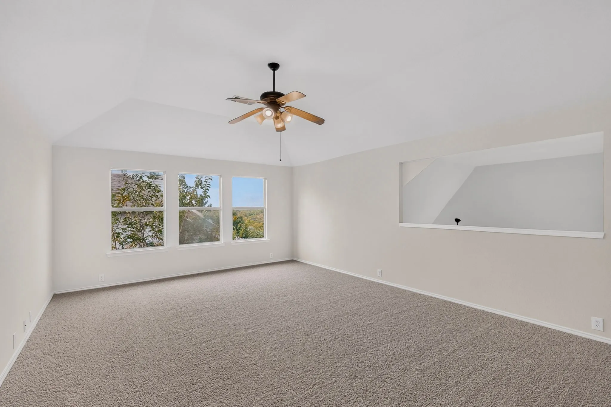 Vaulted ceiling with an attached ceiling fan, three pane windows, neutral wall paint, and plush carpeting