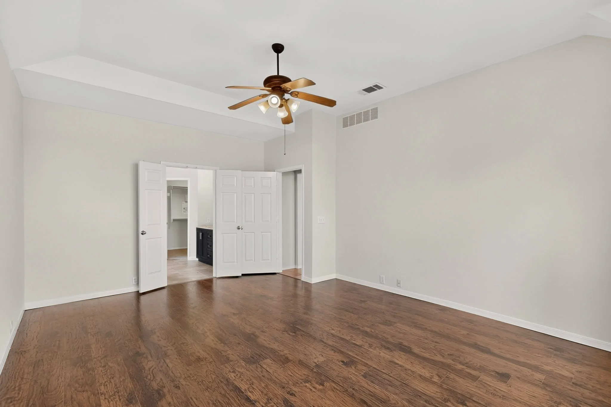 Tray ceiling featuring a ceiling fan with integrated lighting, wood-finish flooring, and white walls