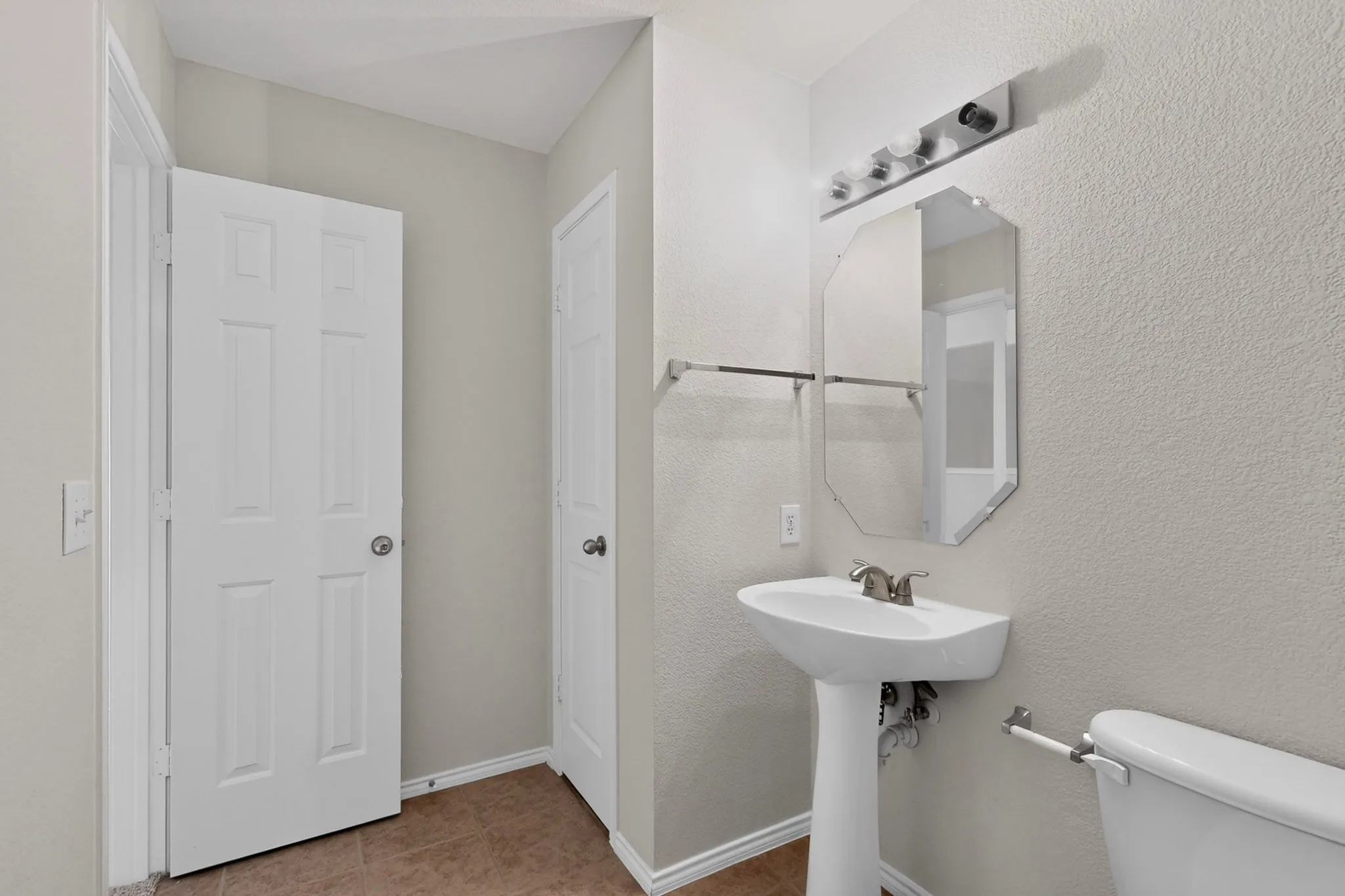 Pedestal sink with a brushed nickel faucet, octagonal mirror, and a four-light vanity fixture