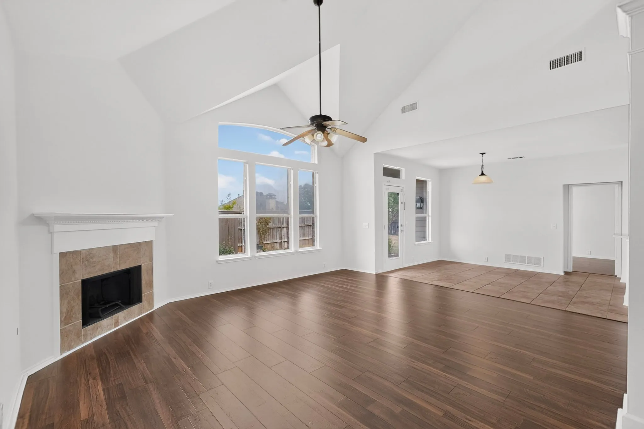 Vaulted ceiling, wood-finish flooring, fireplace with tile surround, large windows, and a ceiling fan