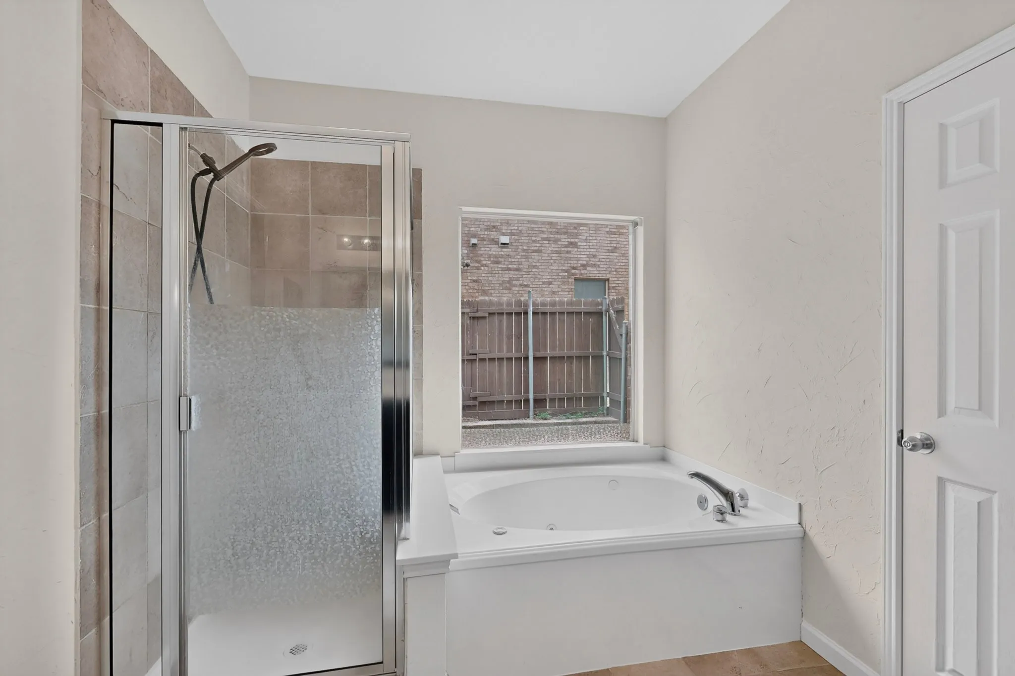 Recessed jetted tub with a window, glass-enclosed shower with tile surround, and a paneled interior door