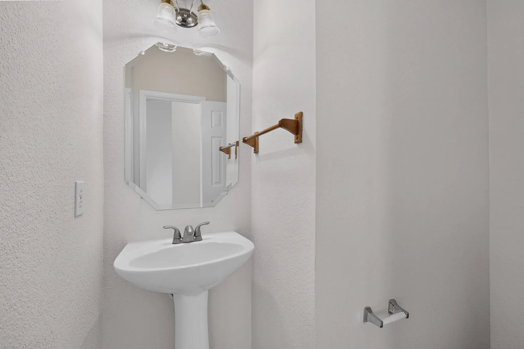 Pedestal sink with chrome faucet, octagonal mirror, and wall-mounted light fixture