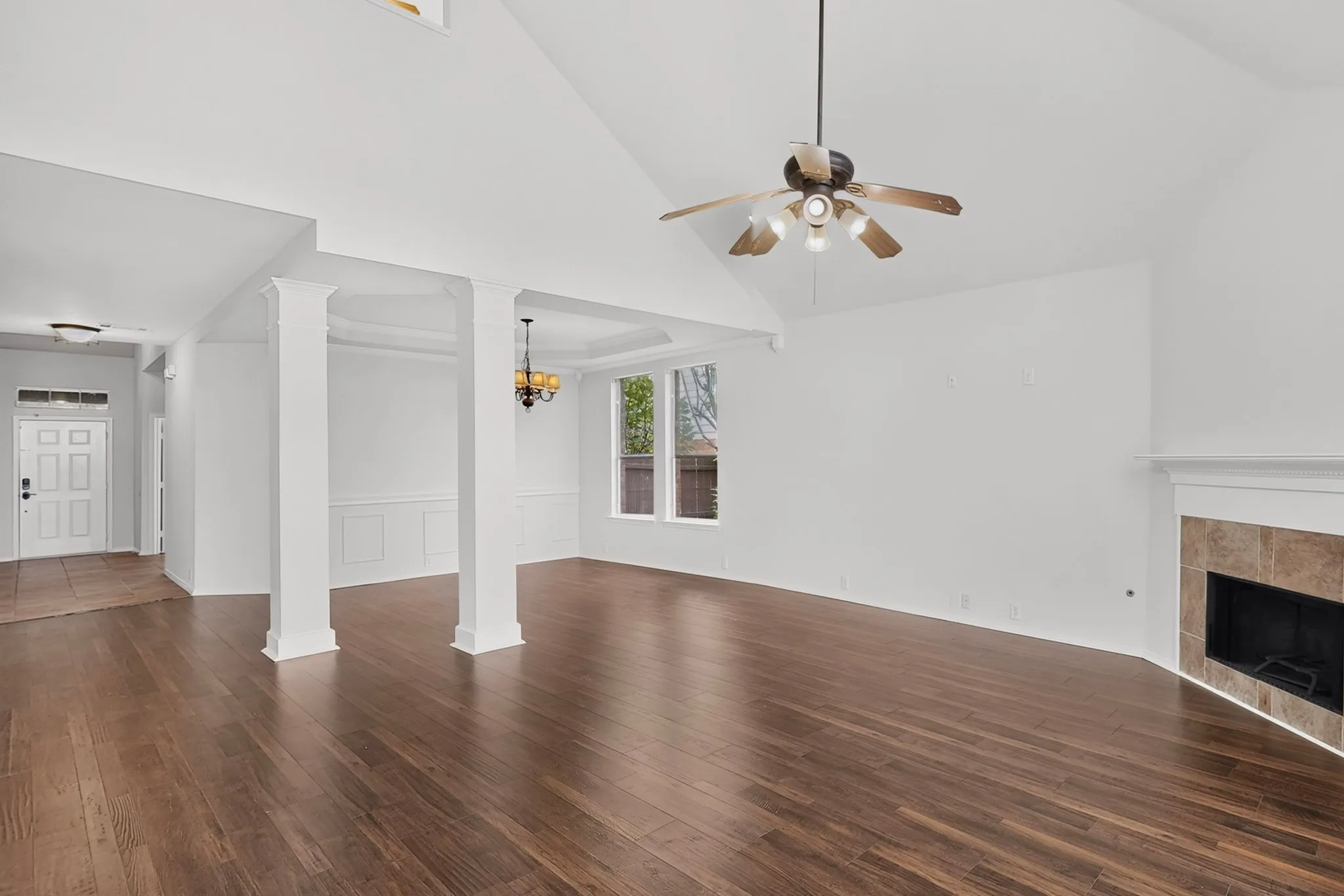 Expansive living area with wood-finish flooring, a tiled fireplace, and a vaulted ceiling with a ceiling fan