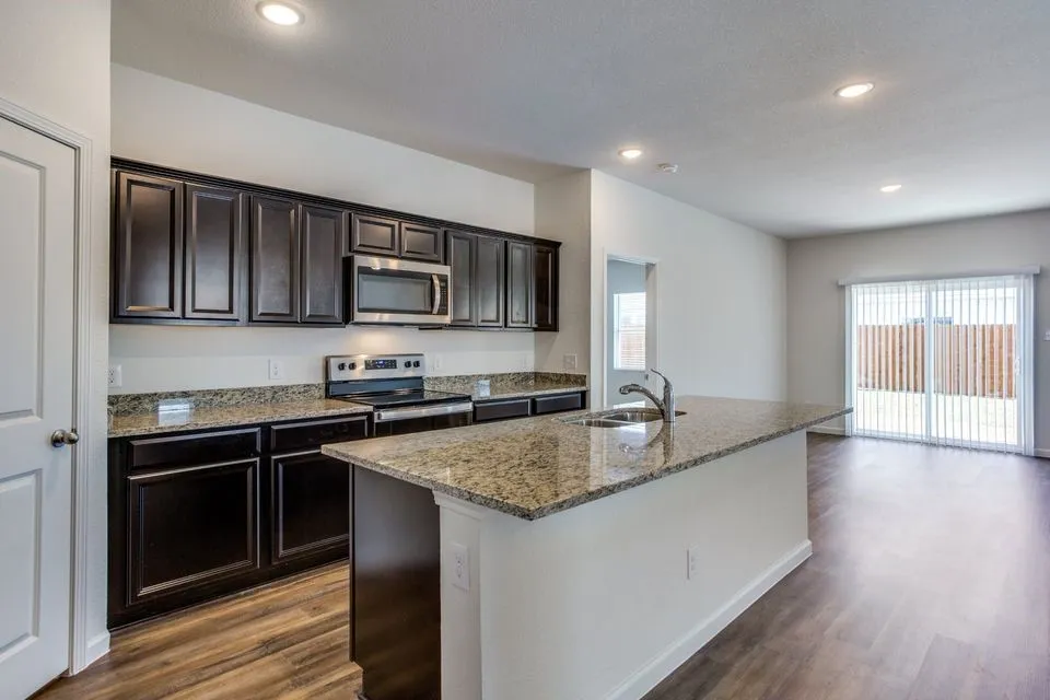 Kitchen featuring dark wood-finish cabinetry, light-colored countertops, stainless steel appliances, a center island with sink, and wood-finish flooring