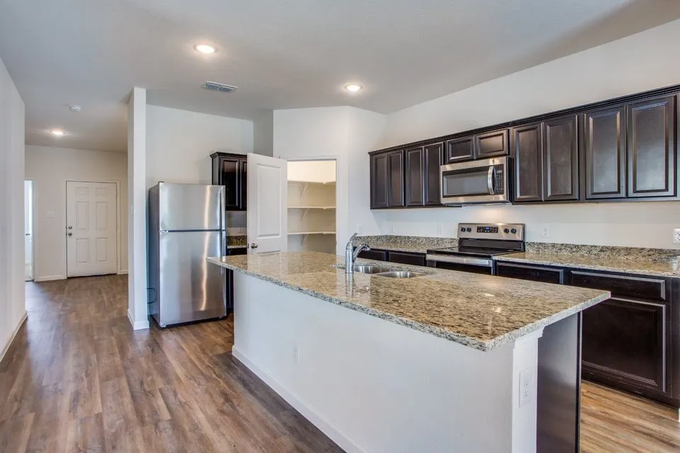Kitchen featuring dark wood-finish cabinetry, granite countertops, stainless steel appliances, and a central island with an undermount sink