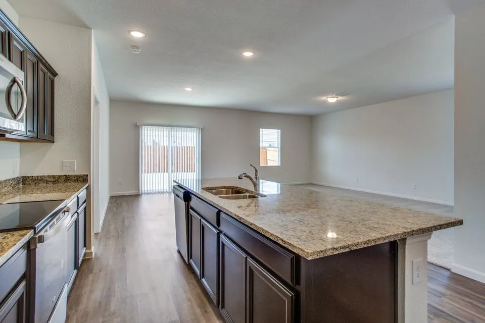 Kitchen featuring an island with a dual-basin sink, granite countertops, wood-finish flooring, recessed lighting, and dark wood cabinetry
