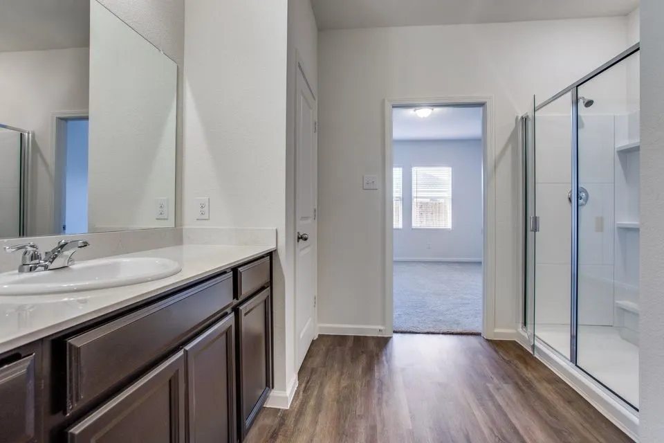 Wood-finish flooring leading to a glass-enclosed shower with integrated shelving