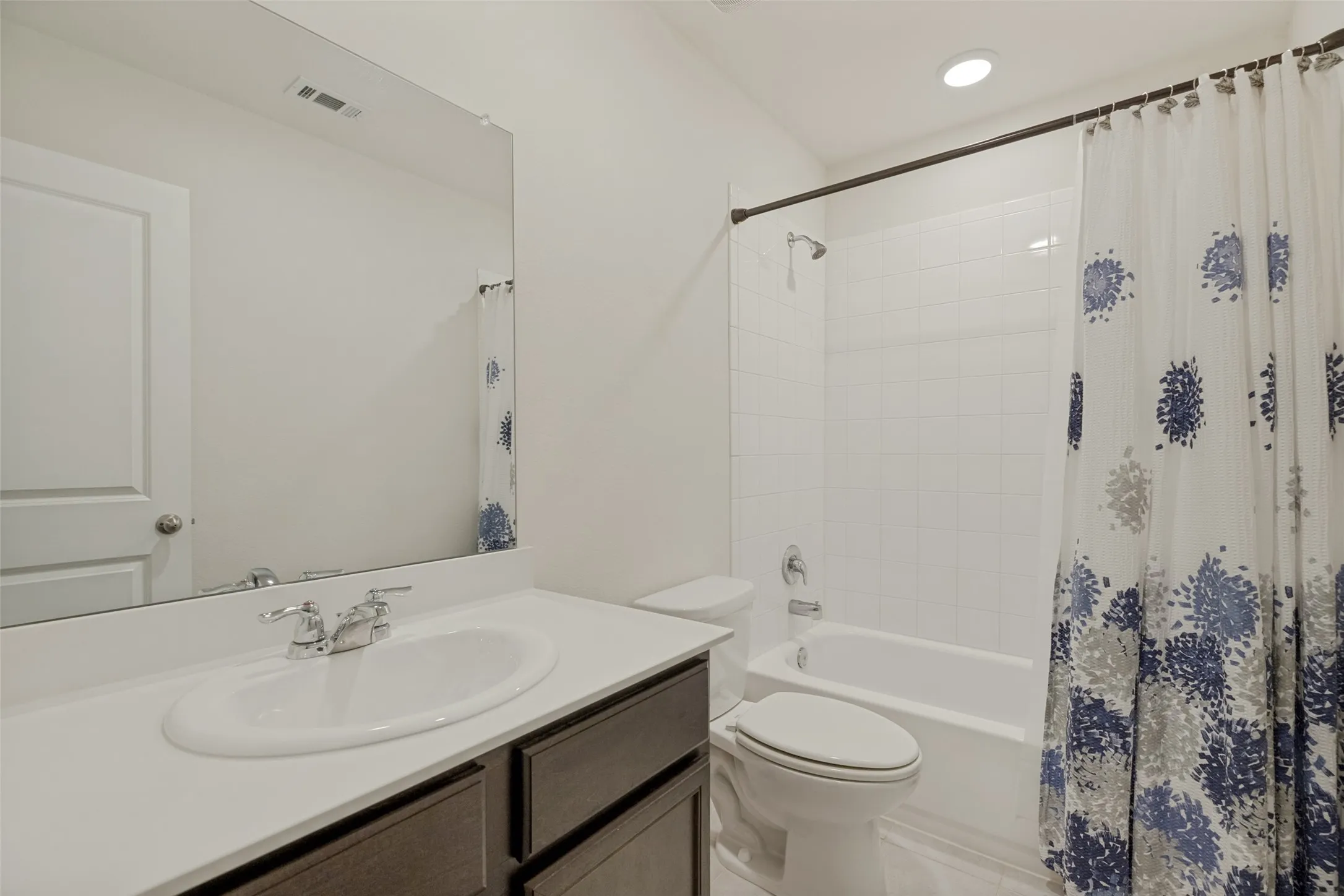 White vanity with an integrated sink, polished chrome faucet, built-in mirror, and white tile tub surround