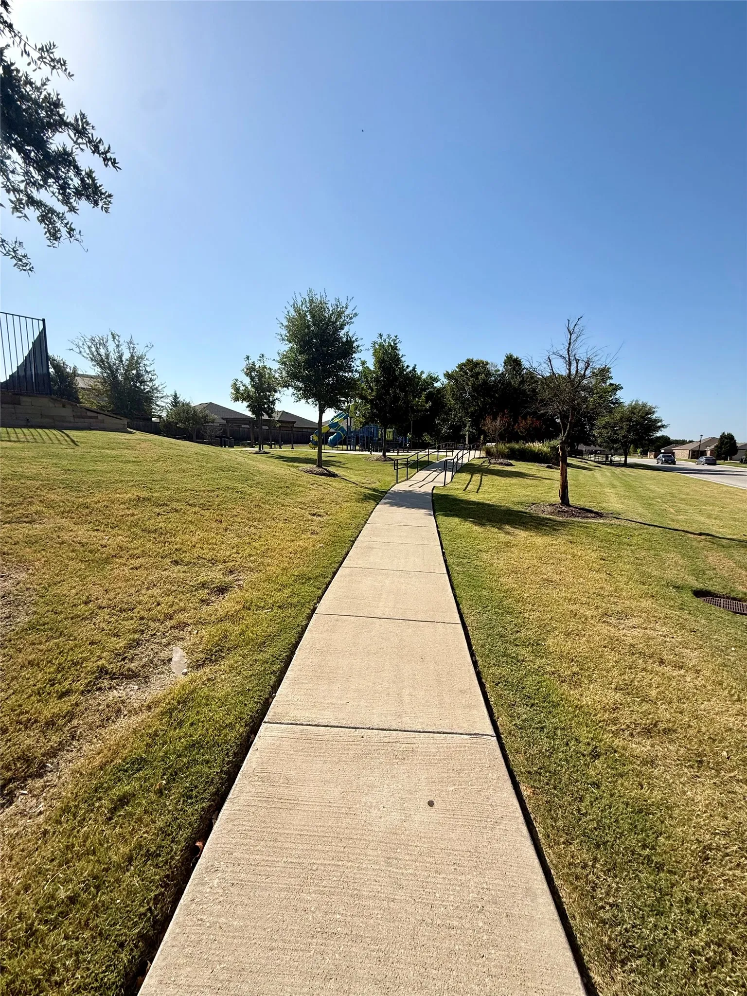 Paved walkway bordered by green grass and established trees