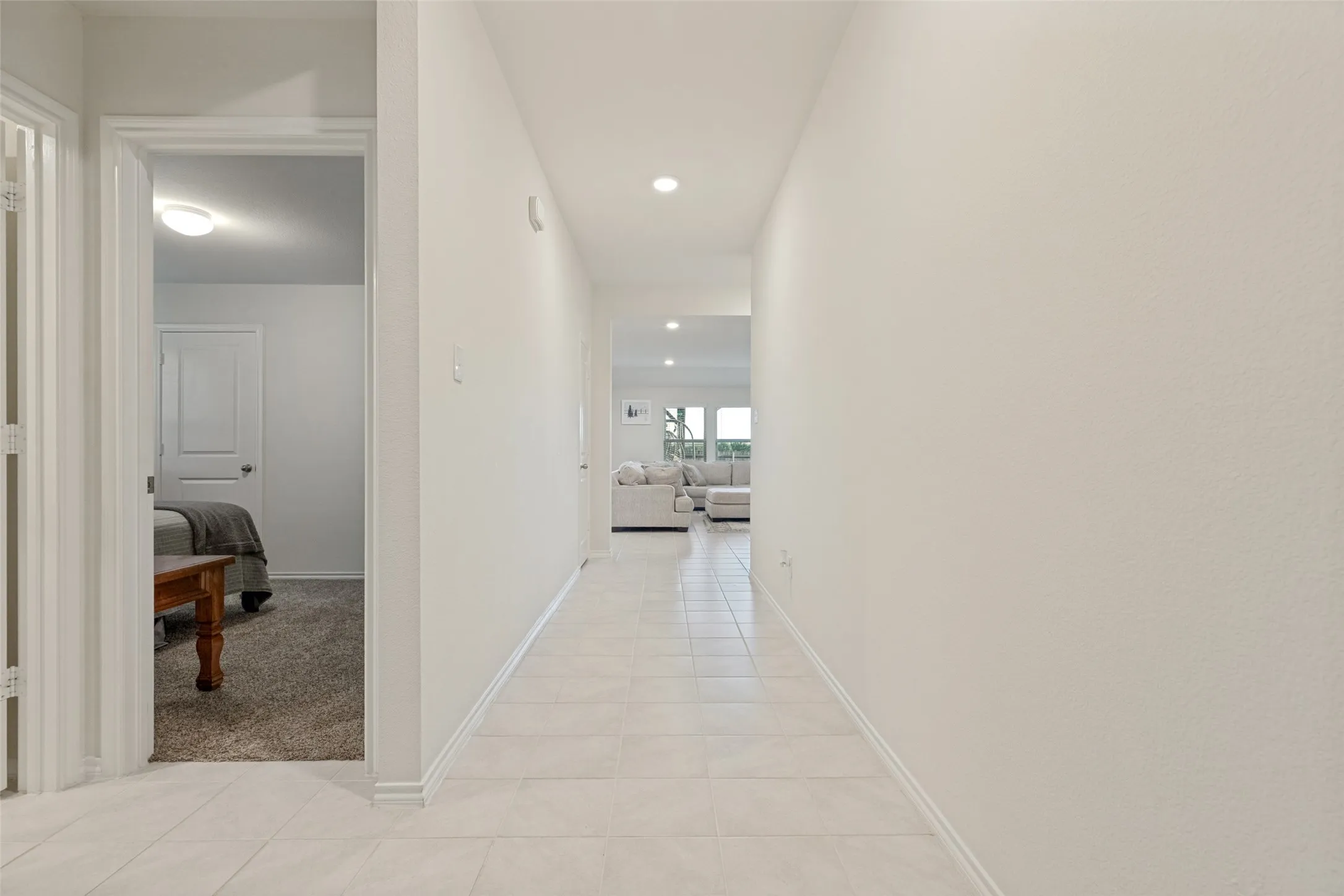 Hallway featuring light-toned tile flooring, recessed ceiling lighting, and a neutral color palette