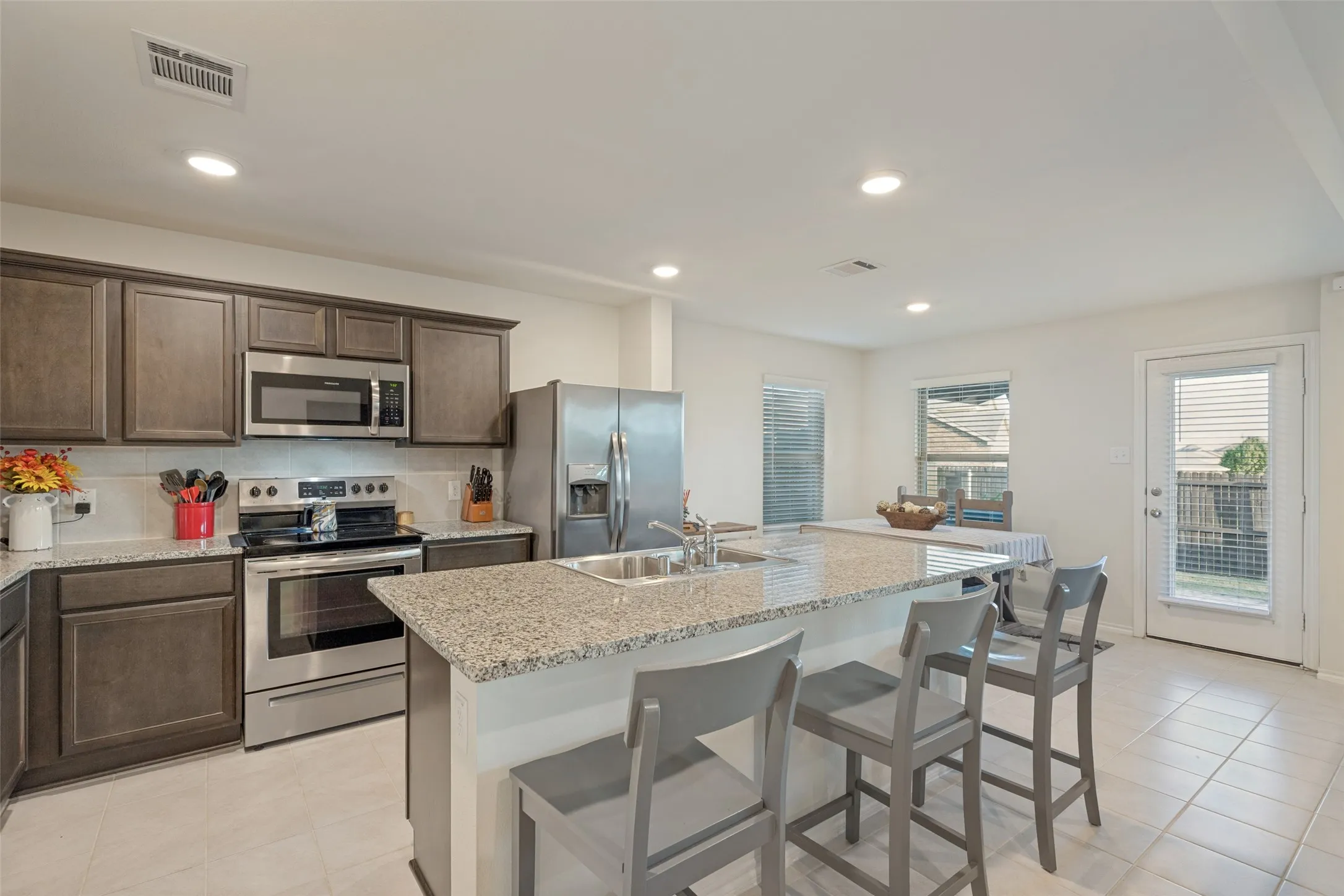 Kitchen featuring stainless steel appliances, dark wood-finish cabinetry, granite countertops, an eat-at island, and tile flooring