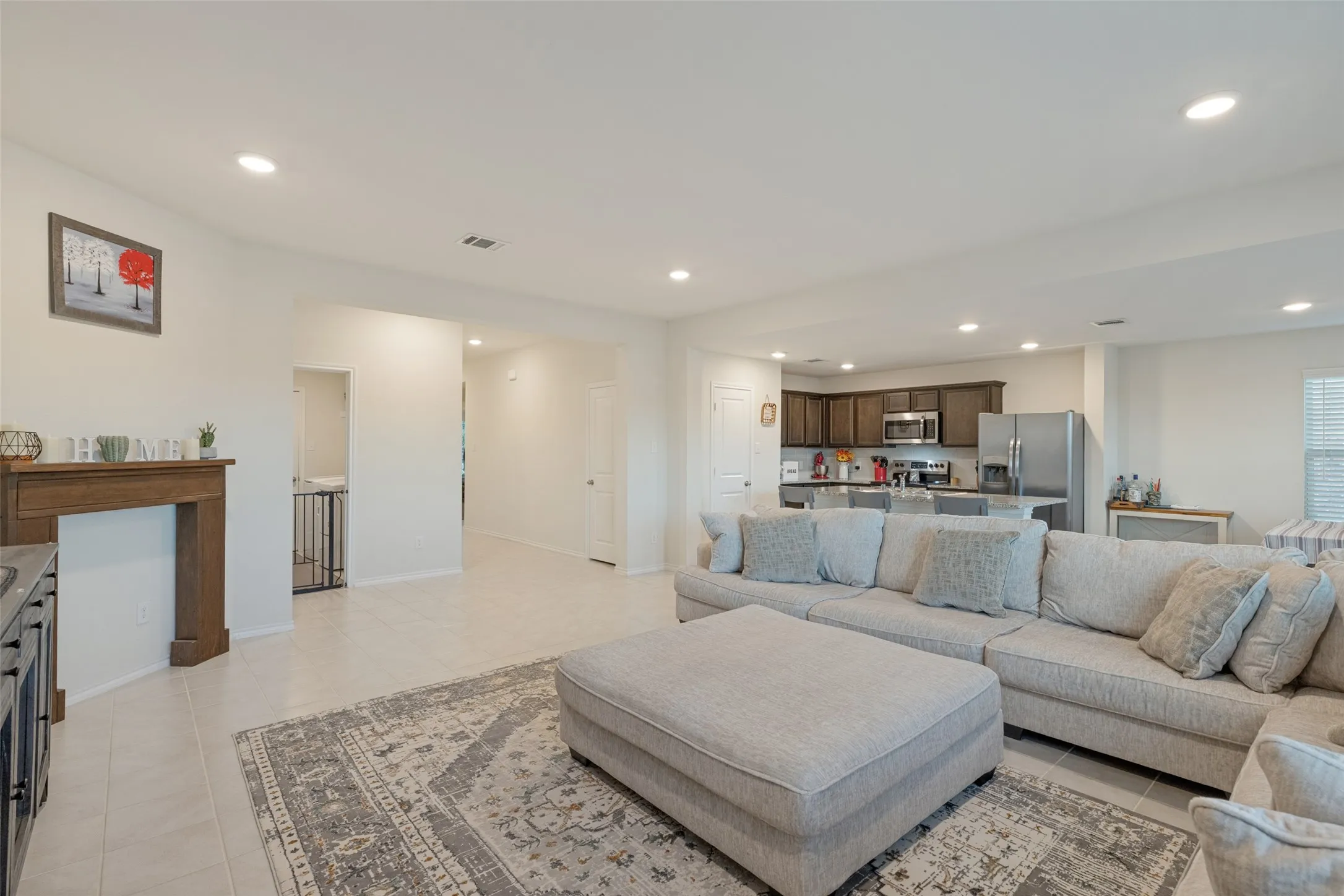 Spacious open-concept living area featuring recessed lighting, tile flooring, and a kitchen with dark wood cabinetry and stainless steel appliances