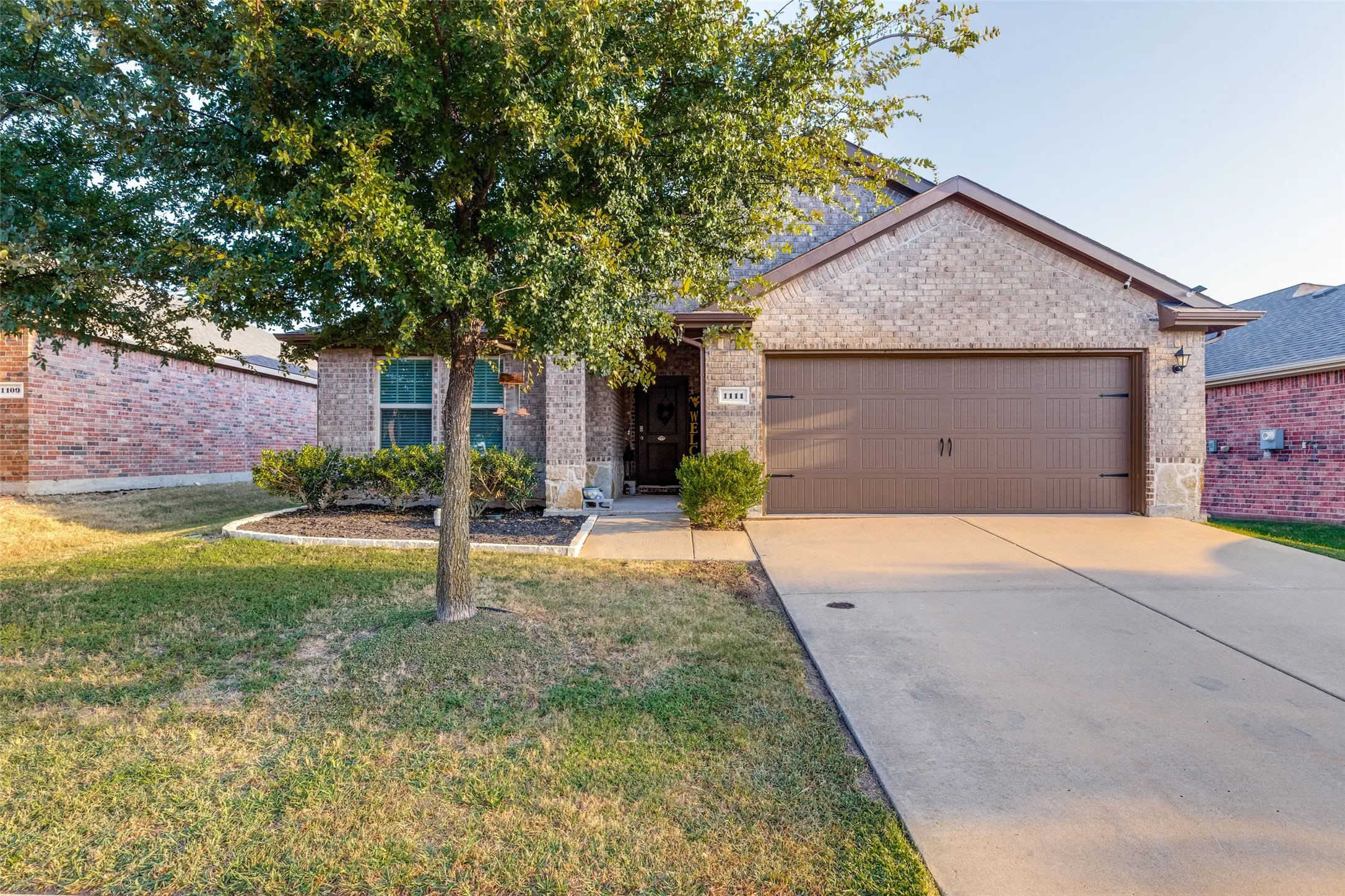Brick and stone exterior with a two-car garage, concrete driveway, and front yard landscaping