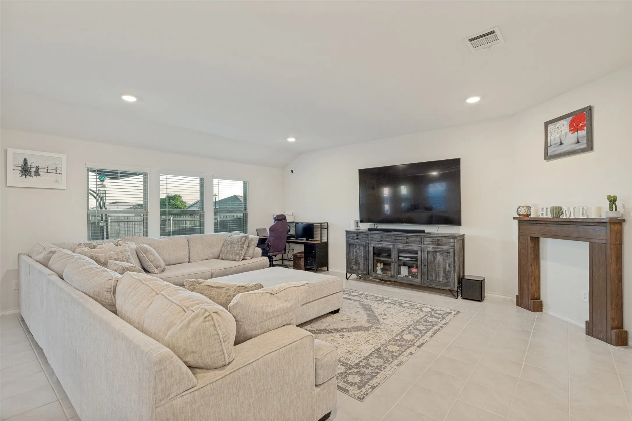 Recessed lighting illuminates the open living area featuring tile flooring, multiple windows, and a decorative wood mantel